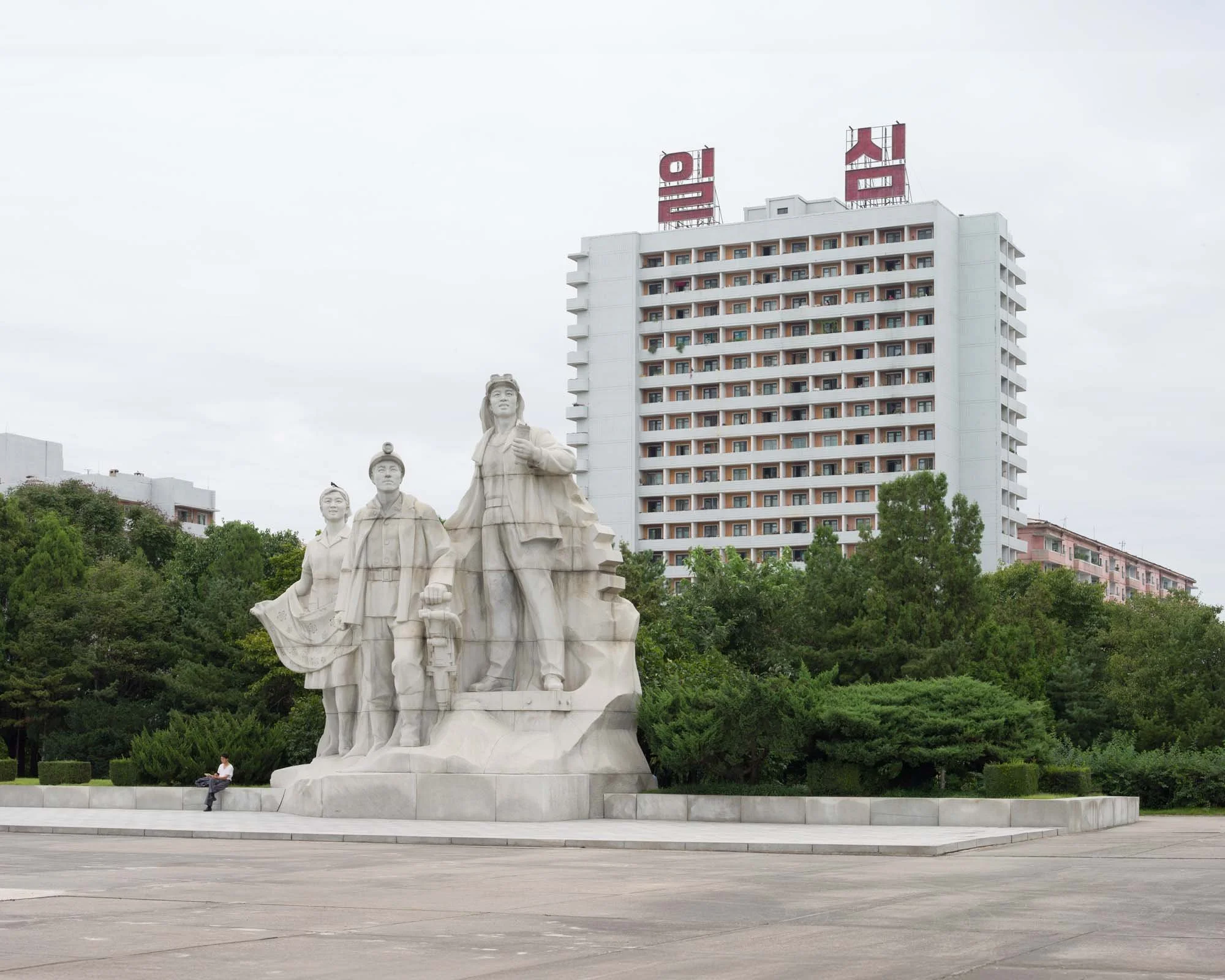 Nebengruppe des Juche-Turms in Pjöngjang, Nordkorea: Eine der begleitenden Granit-Skulpturengruppen, die sich seitlich des zentralen Juche-Monuments befindet. Sie zeigt Repräsentanten des Volkes (Arbeiter, Bauarbeiter und Intellektuelle) in heroische