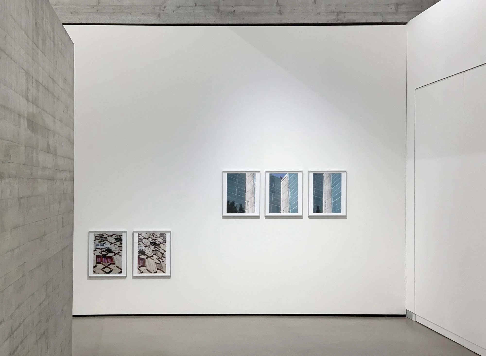 Ein Kunstraum mit weißen Wänden, auf denen mehrere Rahmen mit Fotografien und Kunstwerken hängen, sowie ein Sichtfenster an der oberen Wand.
