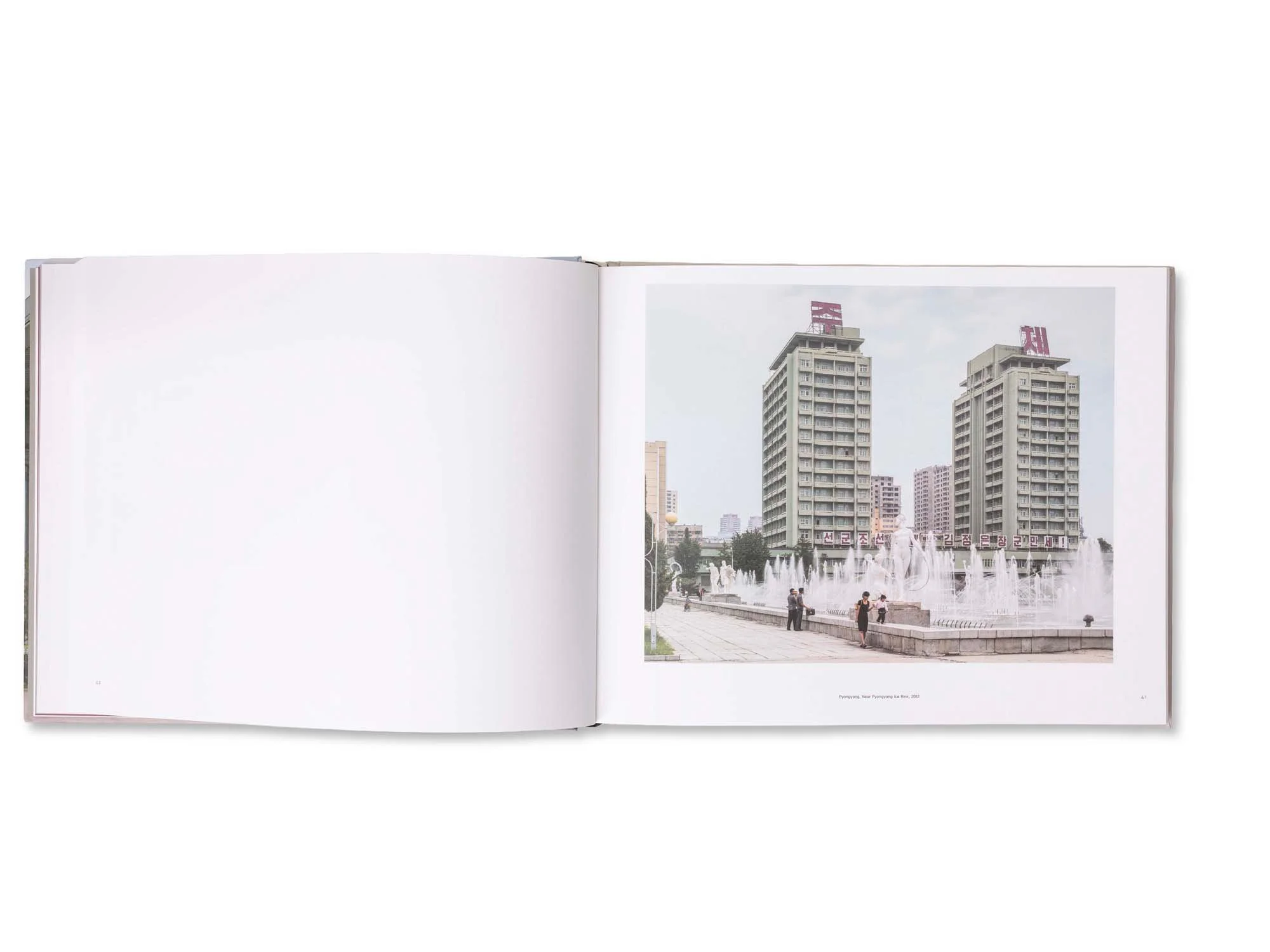 Ein geöffnetes Buch mit einer Fotografie einer Stadt mit hohen Gebäuden und Wasserfontänen im Vordergrund.