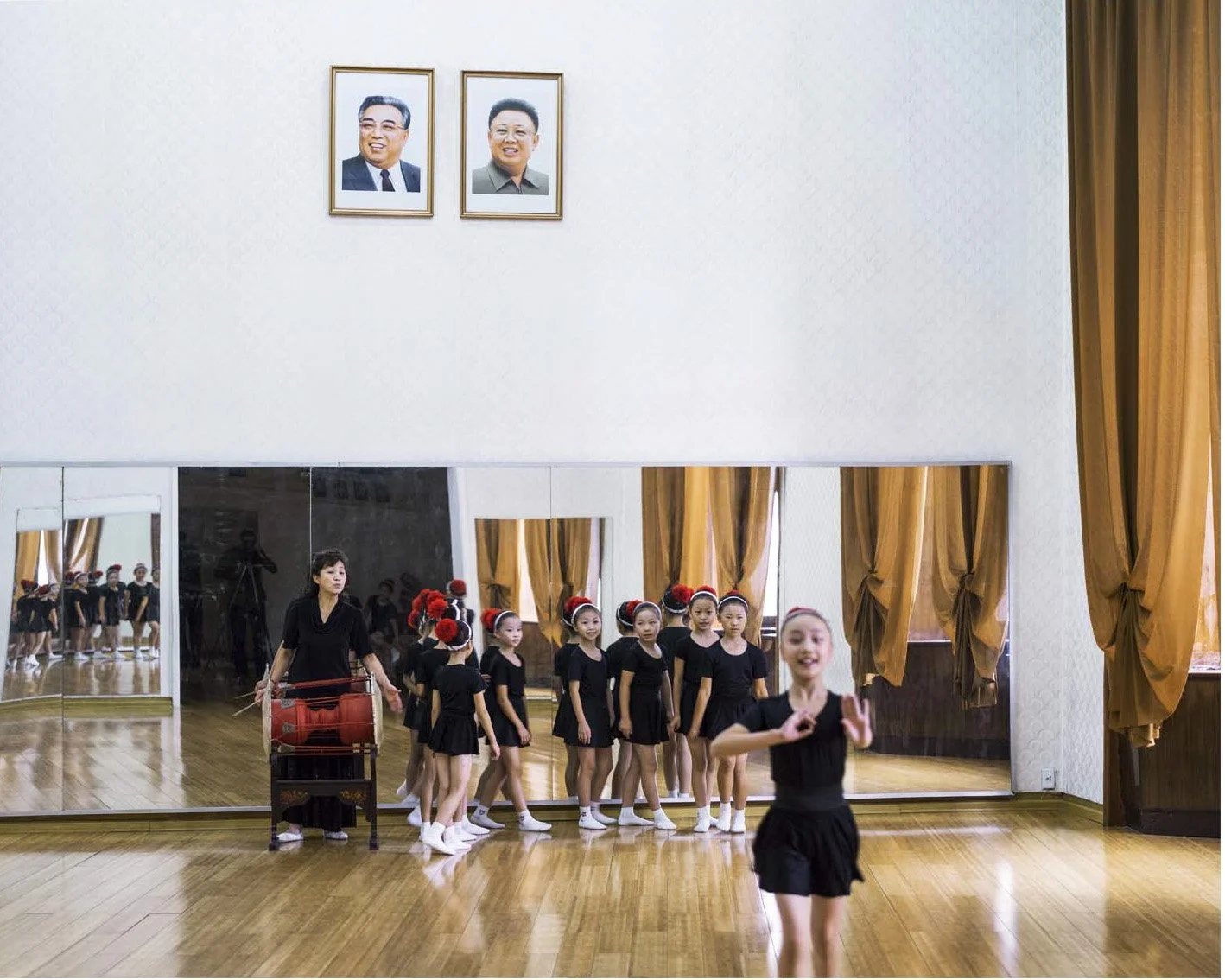 Ballettprobe im Palast des Volkes in Pjöngjang, Nordkorea: Junge Balletttänzerinnen üben gemeinsam mit ihrer Lehrerin in einem Spiegelsaal. An der Wand hängen Porträts von Kim Il-sung und Kim Jong-il.

