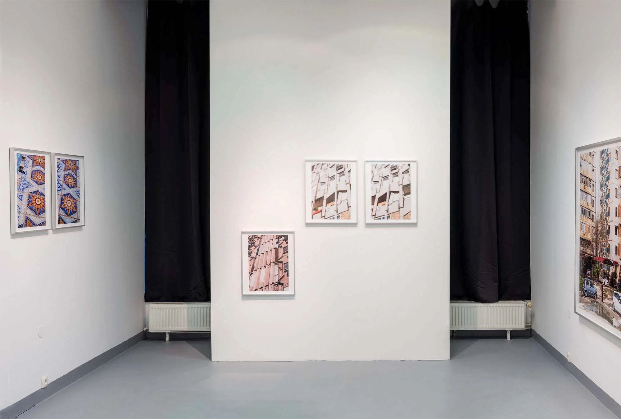 A gallery wall with various framed photographs and artwork, black curtains on either side, and a white partition in the center.