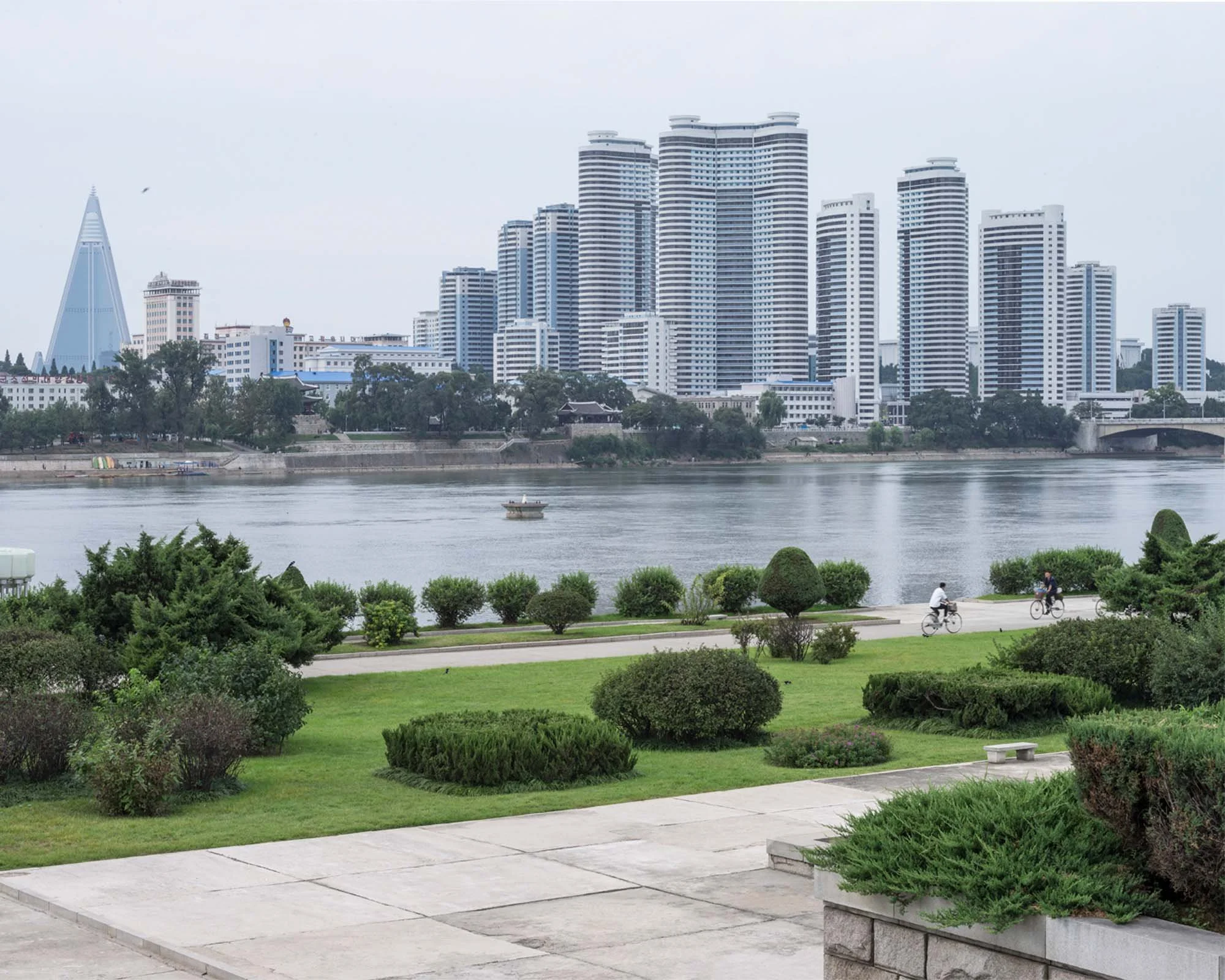 Pjöngjang, Nordkorea – Stadtansicht am Taedong-Fluss mit moderner Skyline, markanten Hochhäusern und grüner Uferpromenade. Die beeindruckende Kombination aus Flusslandschaft, Stadtpark und moderner Architektur zeigt die charakteristische urbane Kulis