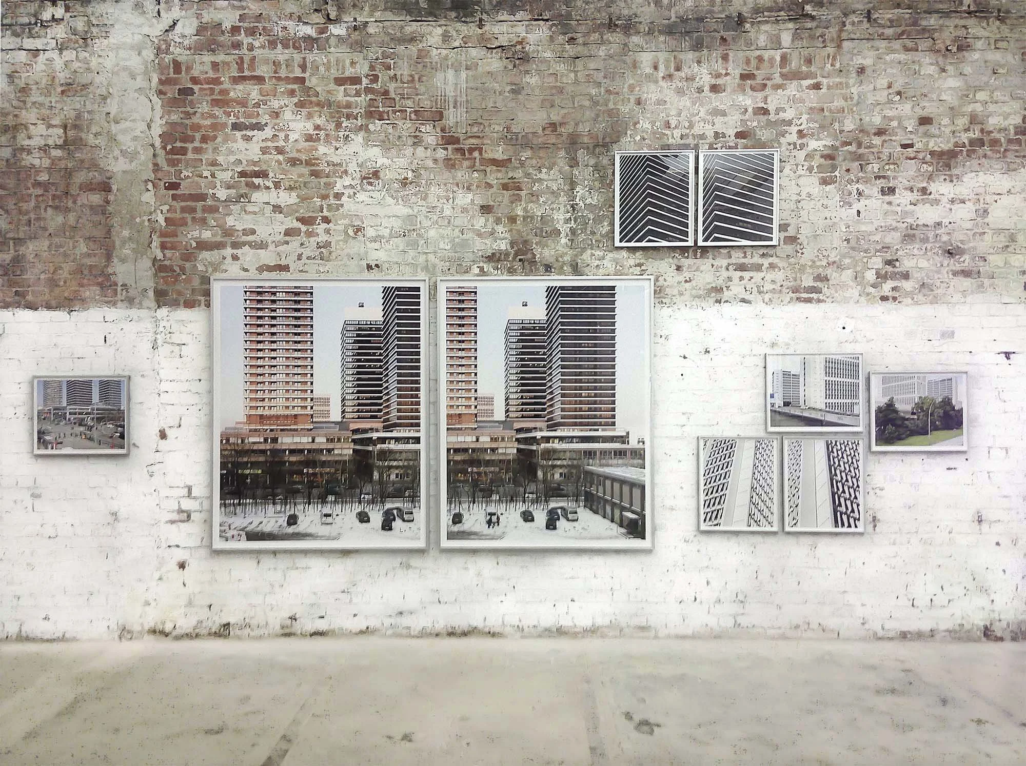 Ein Blick auf eine Wand mit mehreren Rahmenbildern, die Stadtansichten zeigen. Die Wand ist aus rohem Ziegelstein, teilweise gestrichen, mit mehreren kleinen Aircondition-Einheiten.