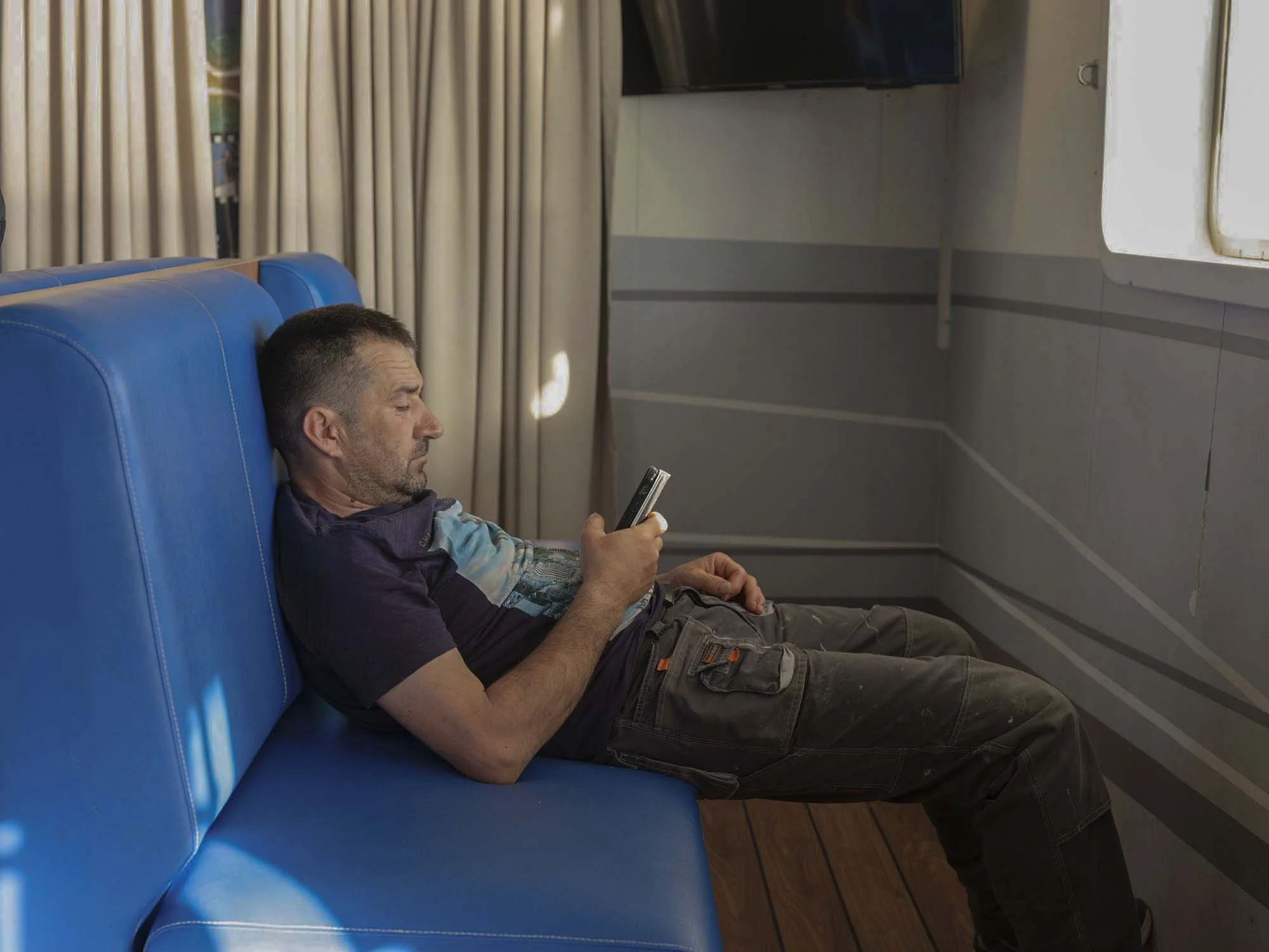 Commuters on the early morning ferry from Split to Brač, Croatia, resting and using smartphones on the deck, documentary photography by Roman Bezjak
