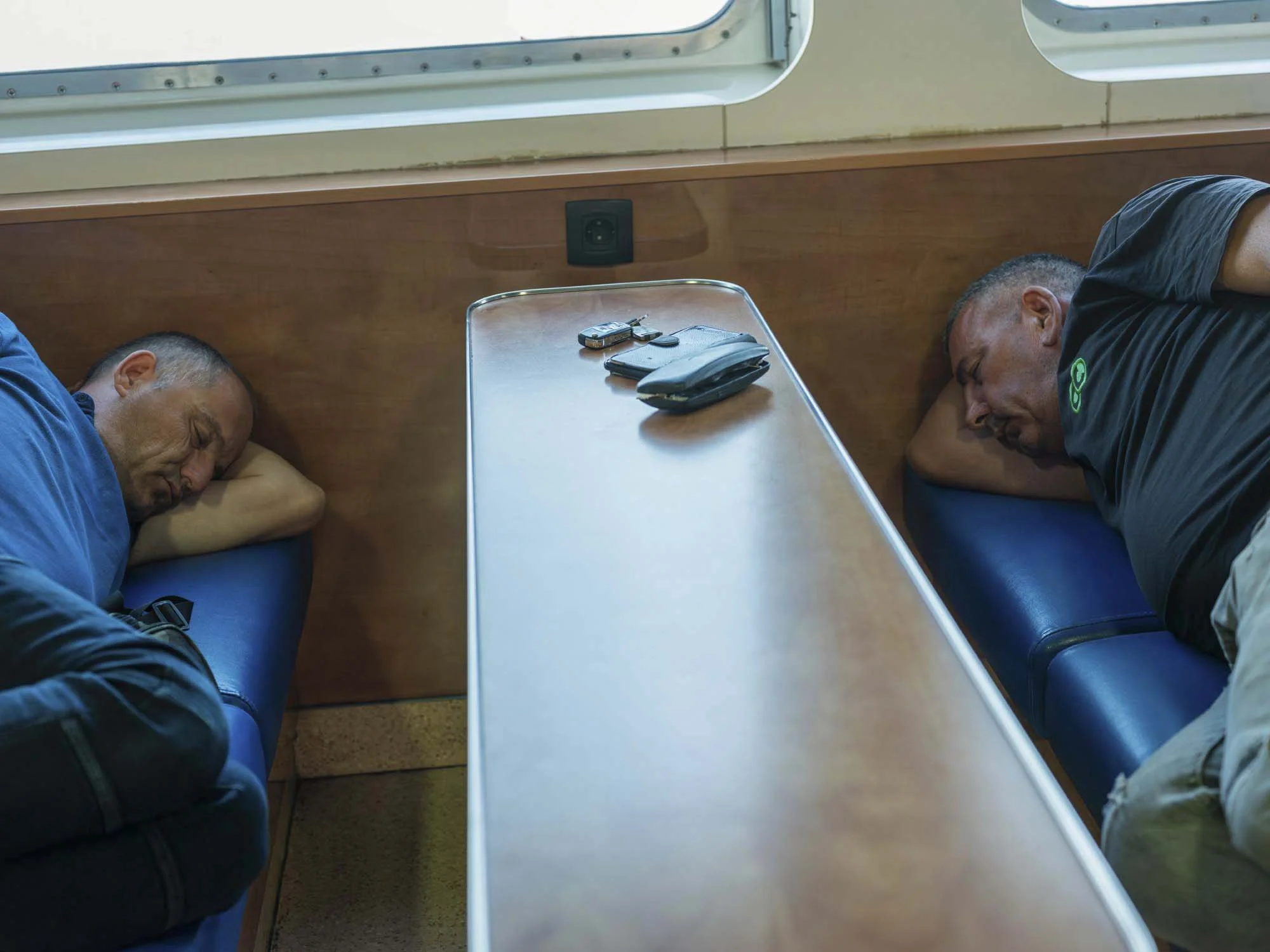 Commuters on the early morning ferry from Split to Brač, Croatia, resting and using smartphones on the deck, documentary photography by Roman Bezjak