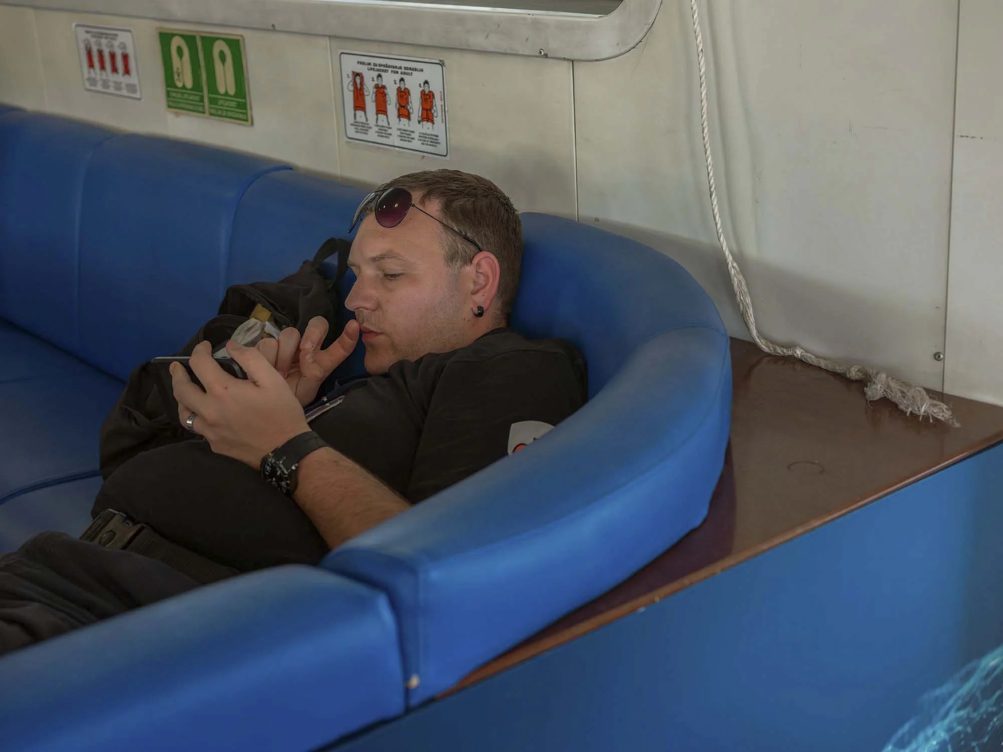 Commuters on the early morning ferry from Split to Brač, Croatia, resting and using smartphones on the deck, documentary photography by Roman Bezjak