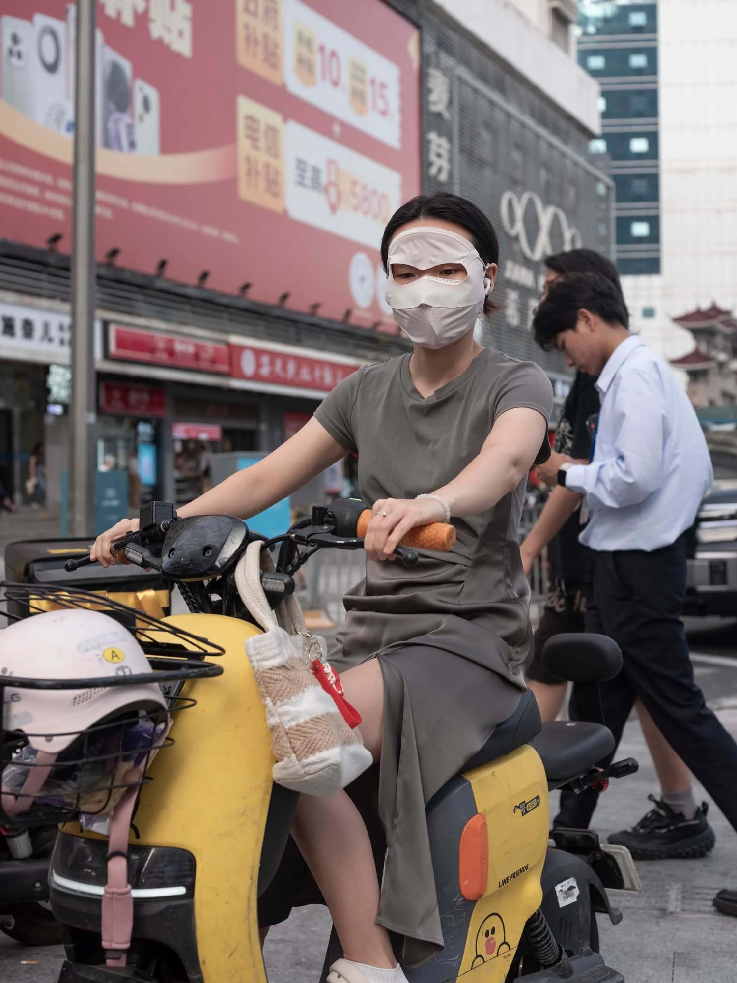 Documentary photograph by Roman Bezjak highlighting Shenzhen as a global leader in e-mobility, showing residents, families, and delivery workers navigating the city on electric scooters. young woman with a mask