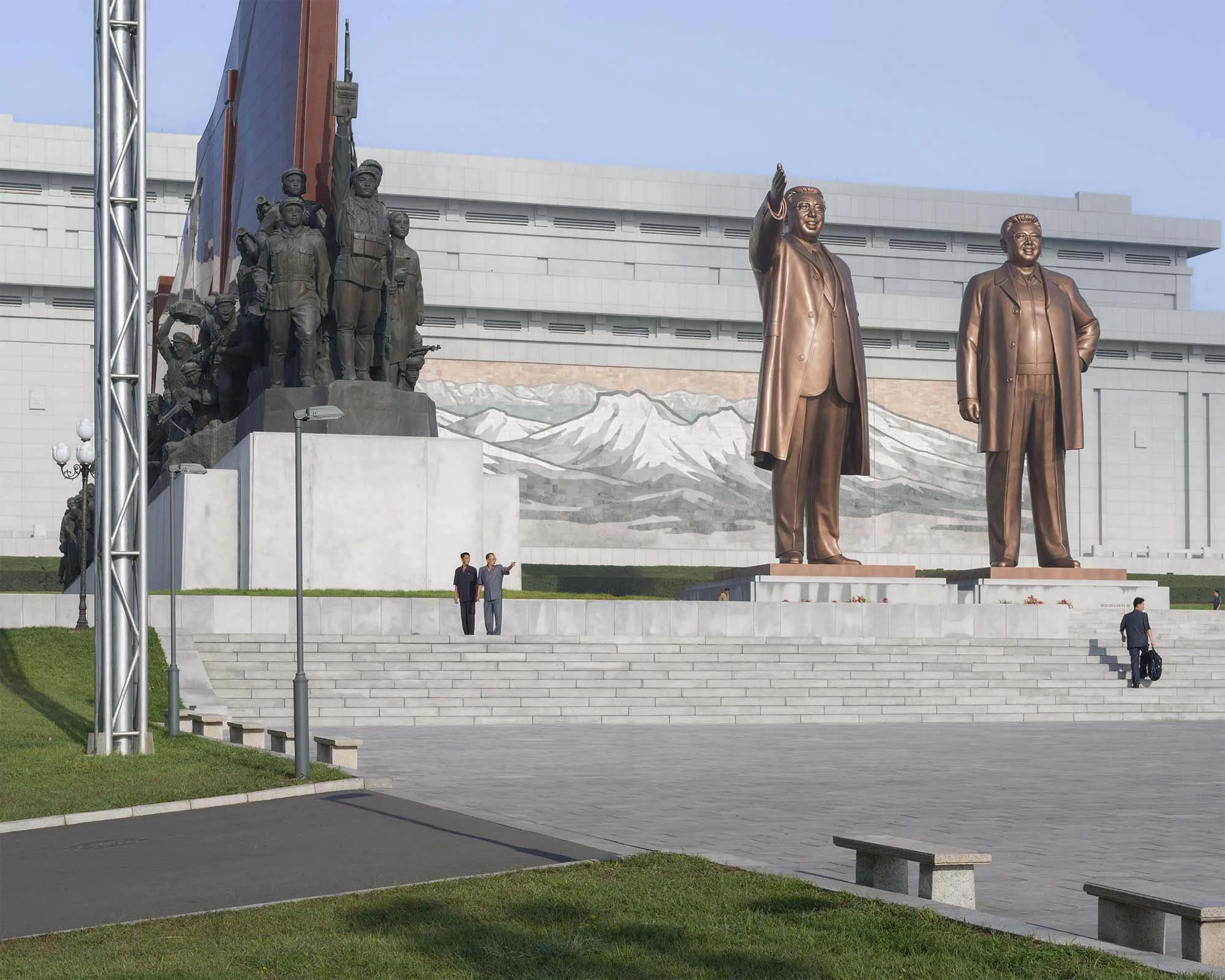Großmonument Mansudae in Pjöngjang, Nordkorea: Die zwei gigantischen Bronzestatuen der verstorbenen Staatsführer Kim Il-sung und Kim Jong-il stehen vor einem Mosaikwandbild des Mount Paektu am Großen Monument Mansudae. Flankiert werden sie von monume