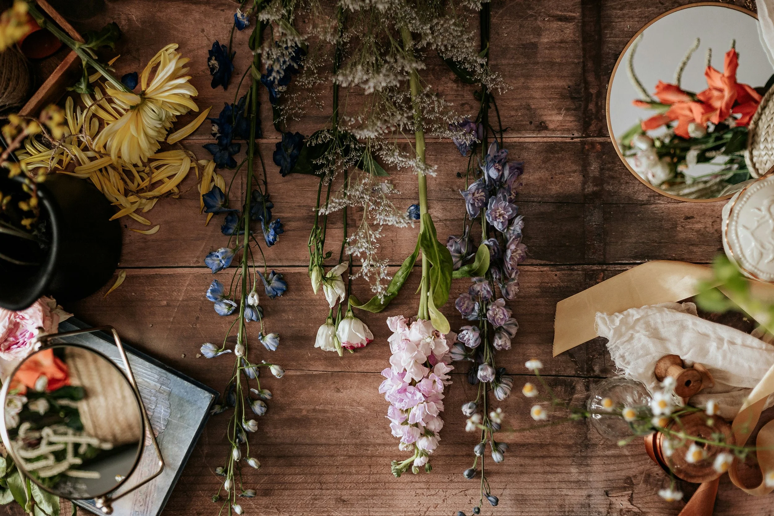 Herbs and flowers arranged on a wooden table with other decorative items.