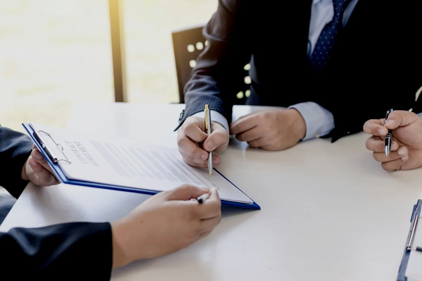 Two people in business suits signing documents on a table during a meeting.