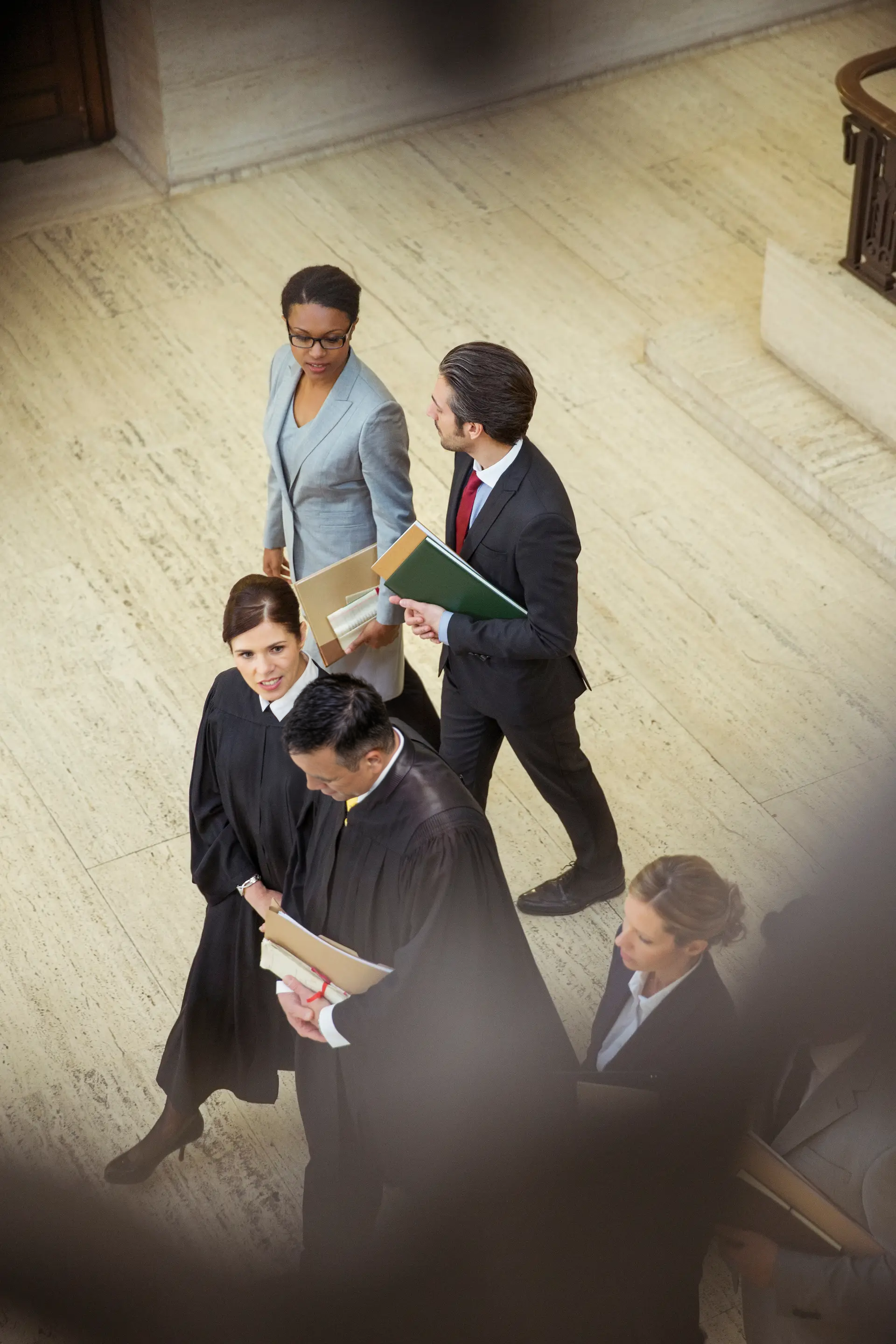 A group of people dressed in formal legal attire, standing in line in what appears to be a courtroom or government building, holding folders and documents.