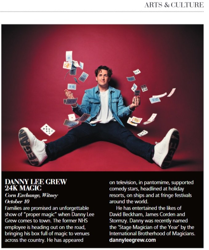 A man in a blue jacket and white sneakers sitting on the floor with legs spread apart. He is surrounded by flying playing cards and banknotes against a red background. The top right corner shows a section of text titled 'Arts & Culture'.