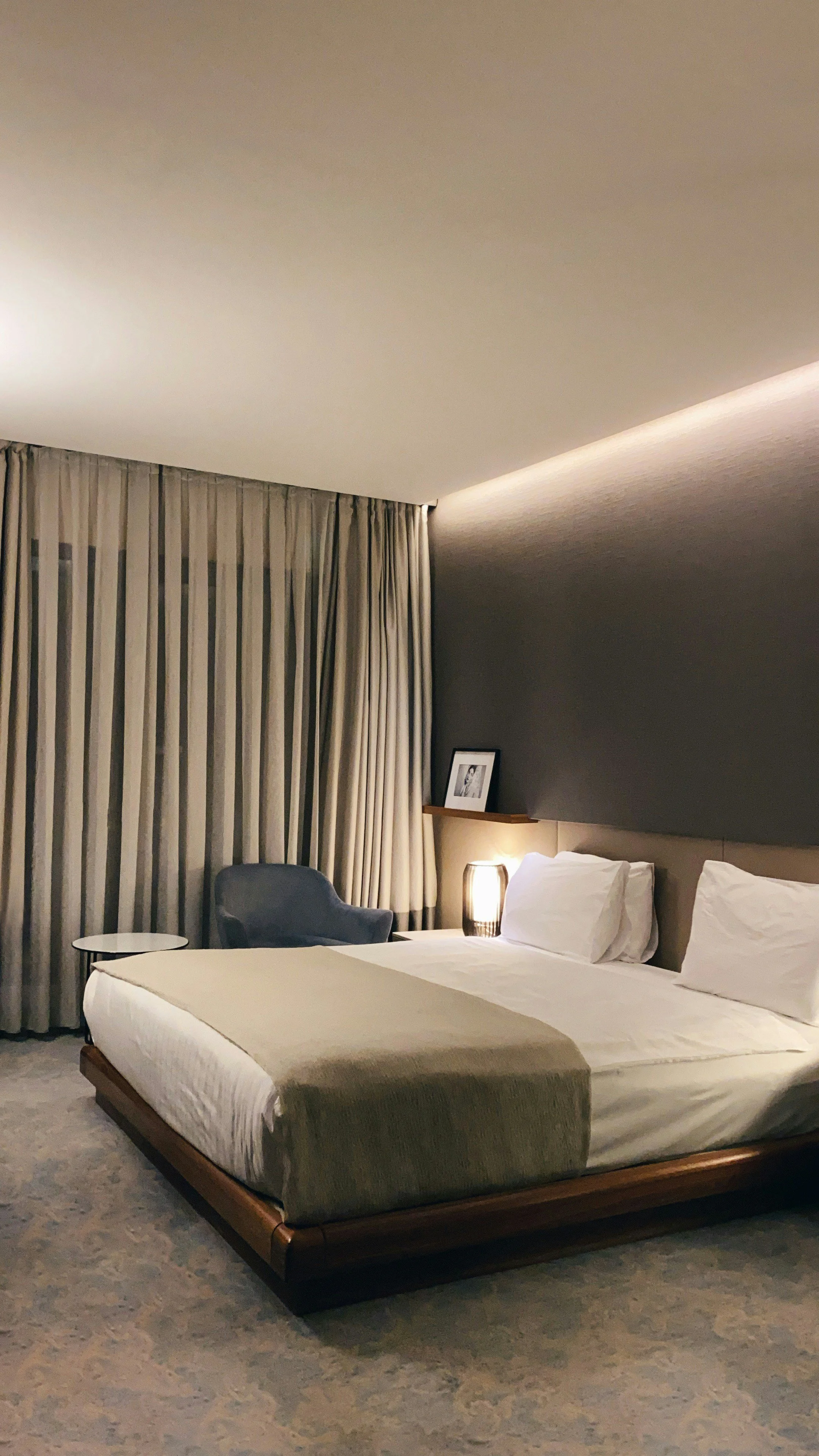Camera da letto moderna con letto matrimoniale, cuscini e lampada a fioca. Pareti colorate, tende lunghi e un quadro appoggiato sulle mensole.