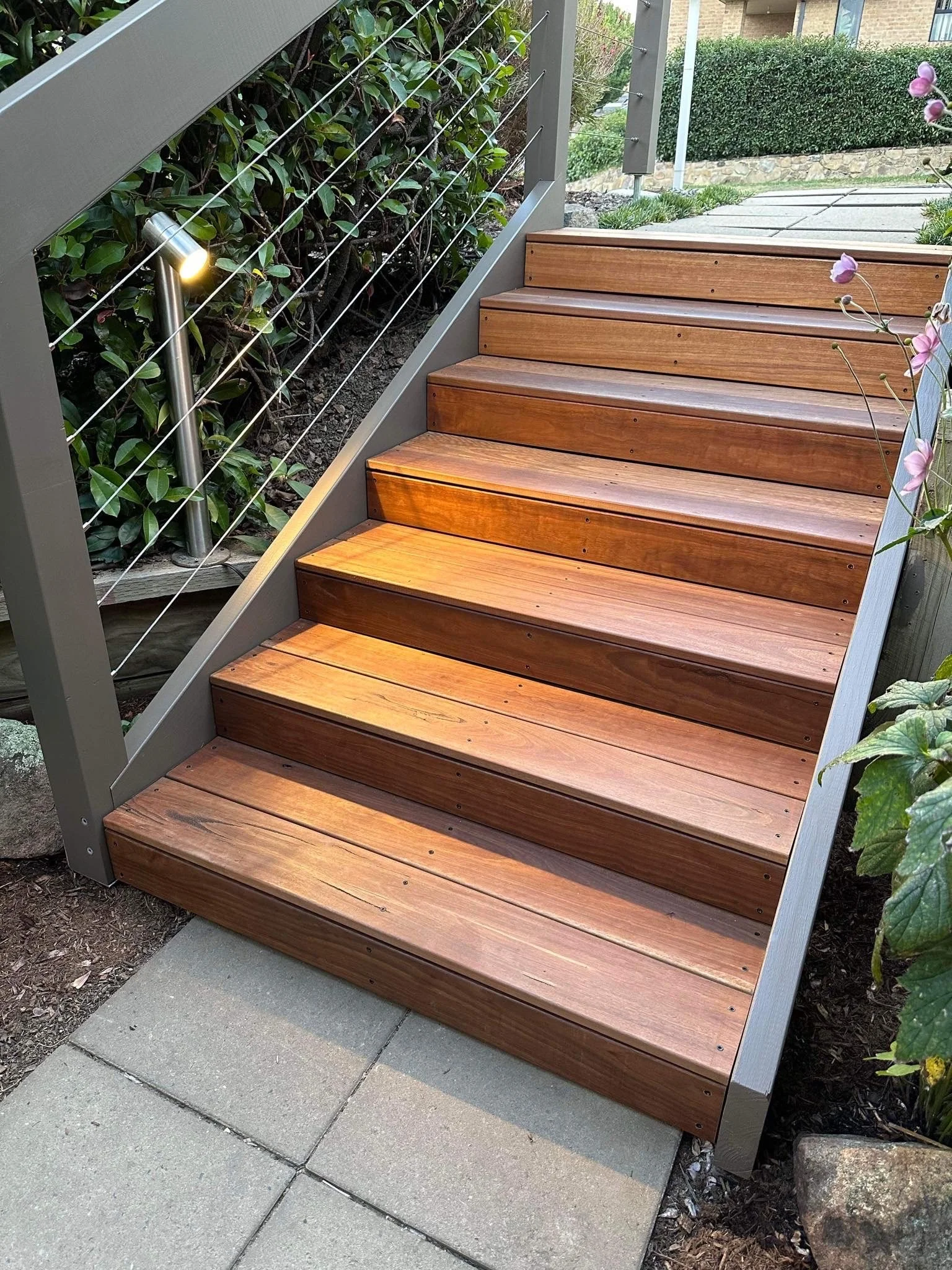 Hardwood stairs installed in a backyard, perfectly complimenting the landscaping of this property. LED lights offer an inviting and modern finish.