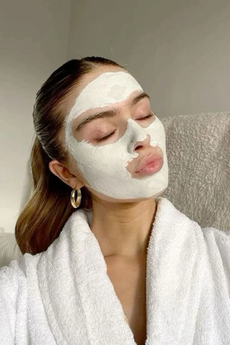 Woman with her eyes closed, relaxing, wearing a white towel and a face mask.