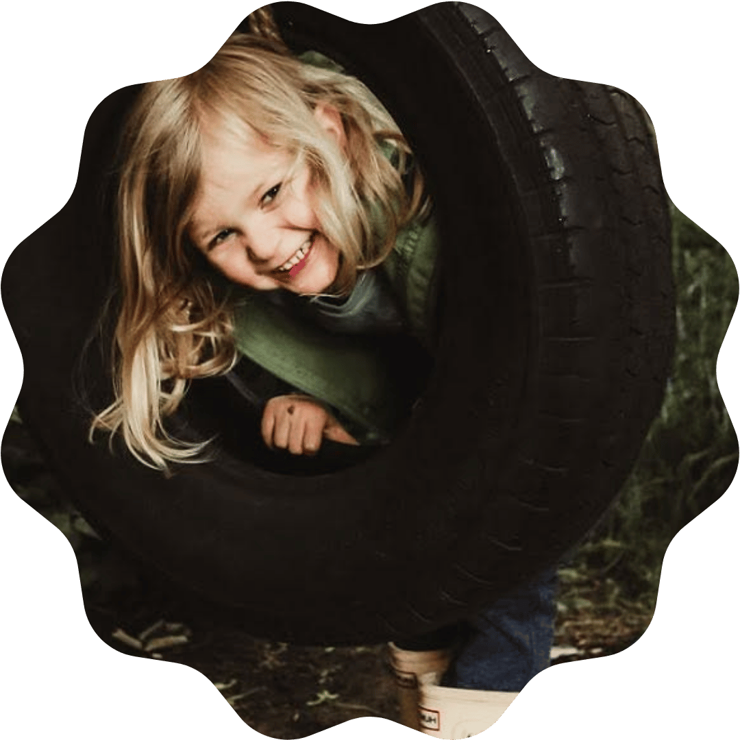 Young girl with blonde hair smiling and playing inside a large black car tire.