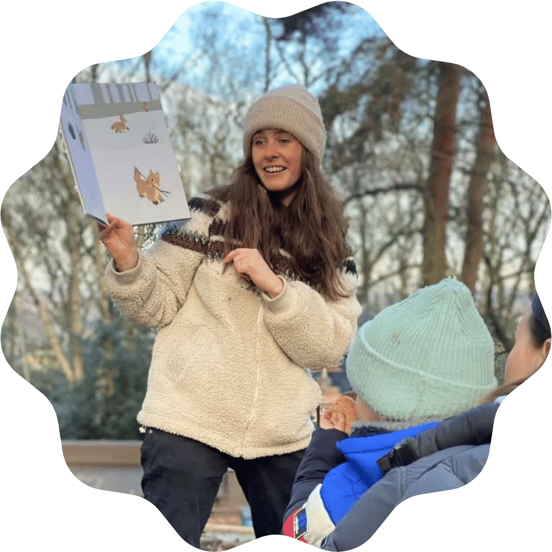 A woman reading a children's book about animals outdoors, with a young child in a green hat and blue jacket listening.