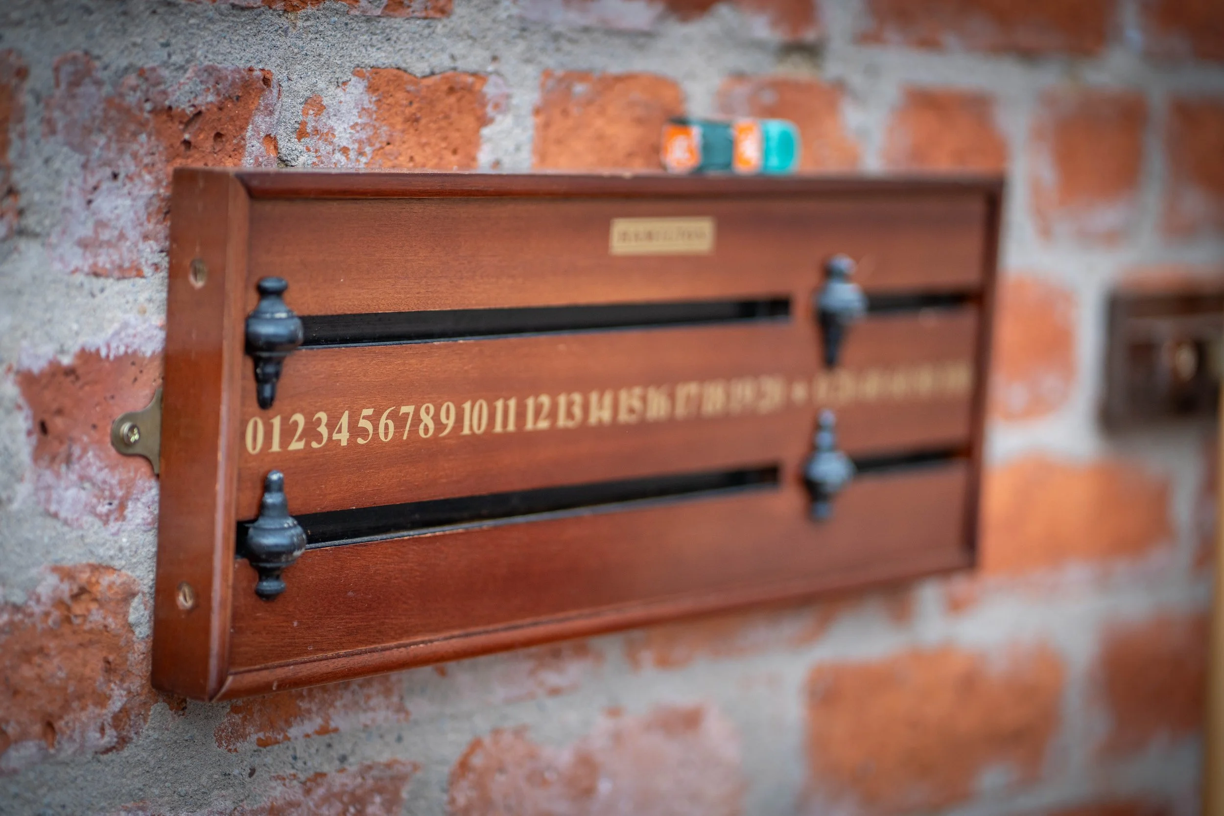 A wooden postal box mounted on a brick wall, with a row of coin slots numbered 0 to 15 and a gold plaque on the front.