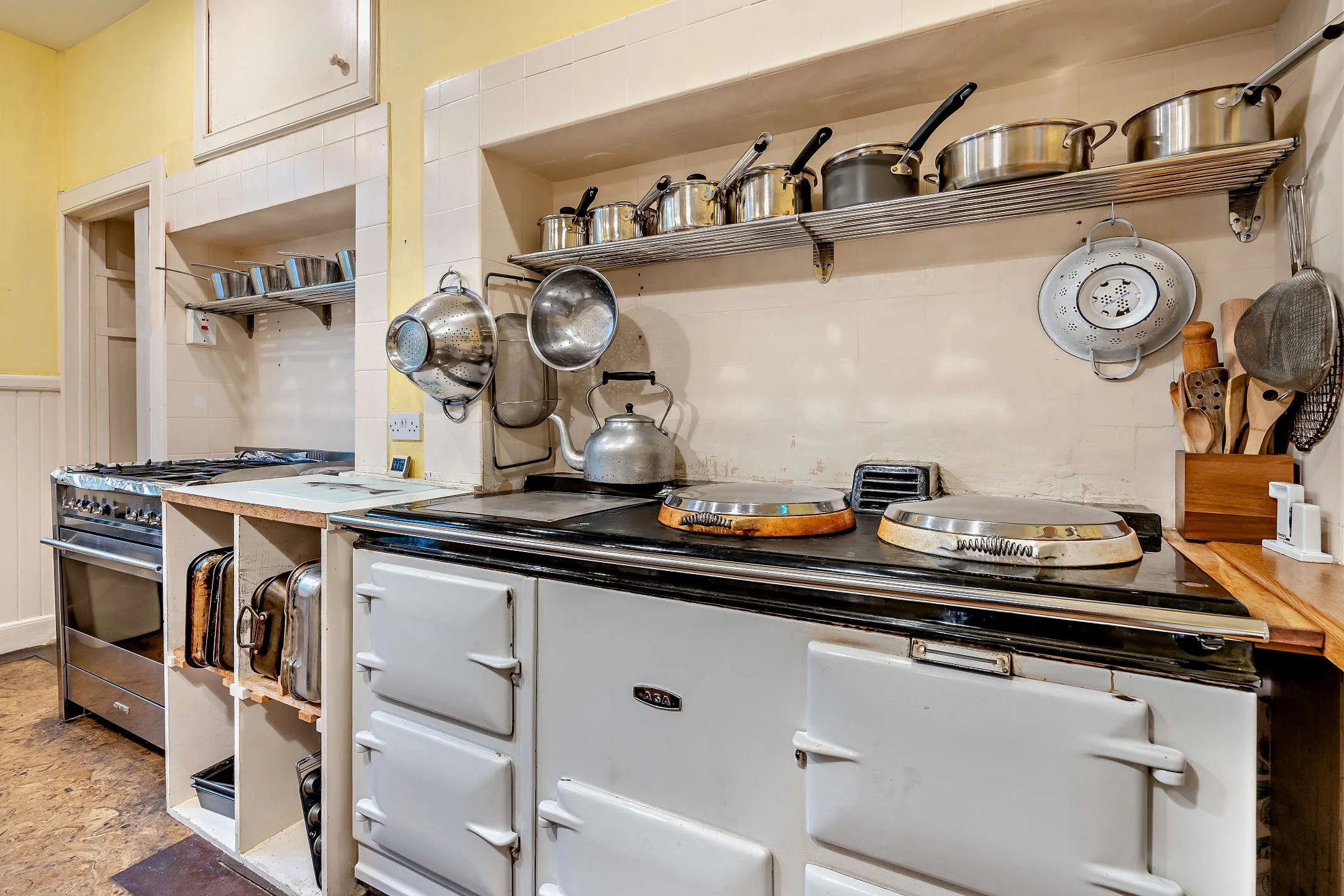 A kitchen with a white vintage stove, a wooden counter, and a wall-mounted shelf holding various pots and kitchen utensils.