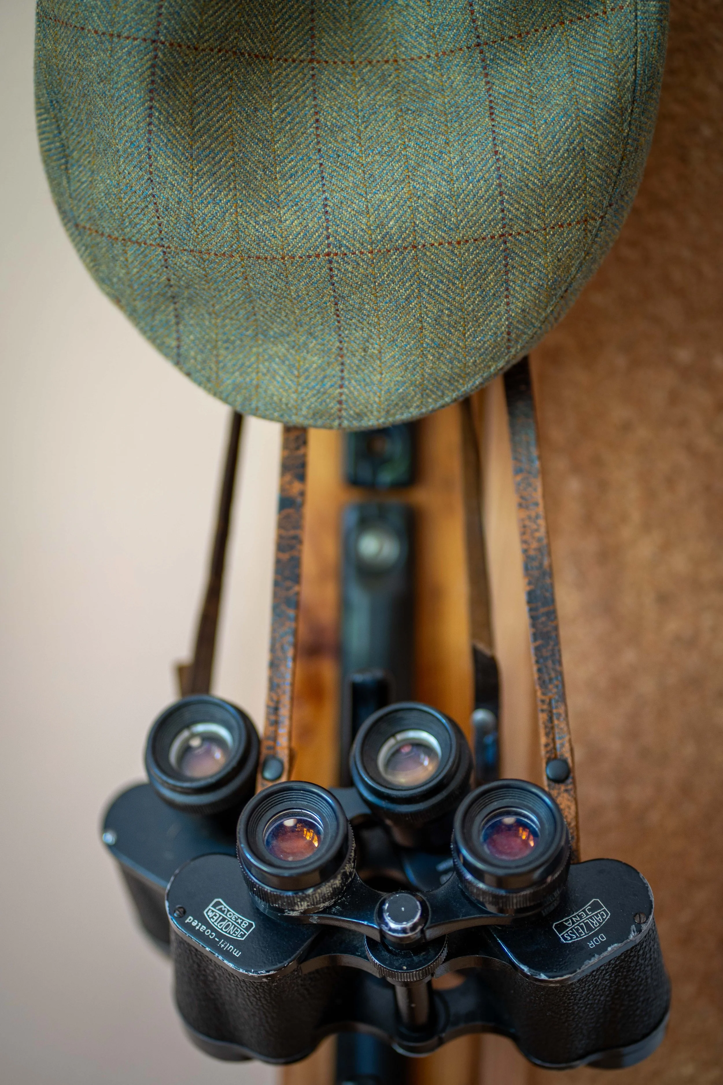 A set of black binoculars with four eyepieces, resting on a wooden stand with a checkered fabric chair above it.