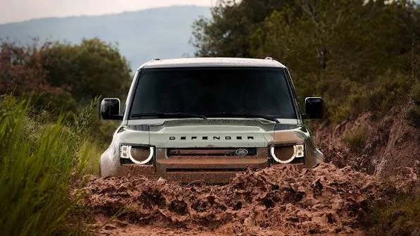 A gray Ford Bronco driving through a muddy off-road trail surrounded by trees and bushes.