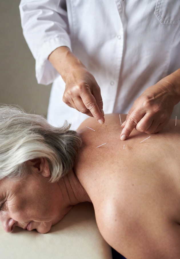 Chiropractor performing acupuncture on an elderly woman's upper back in a clinical setting.