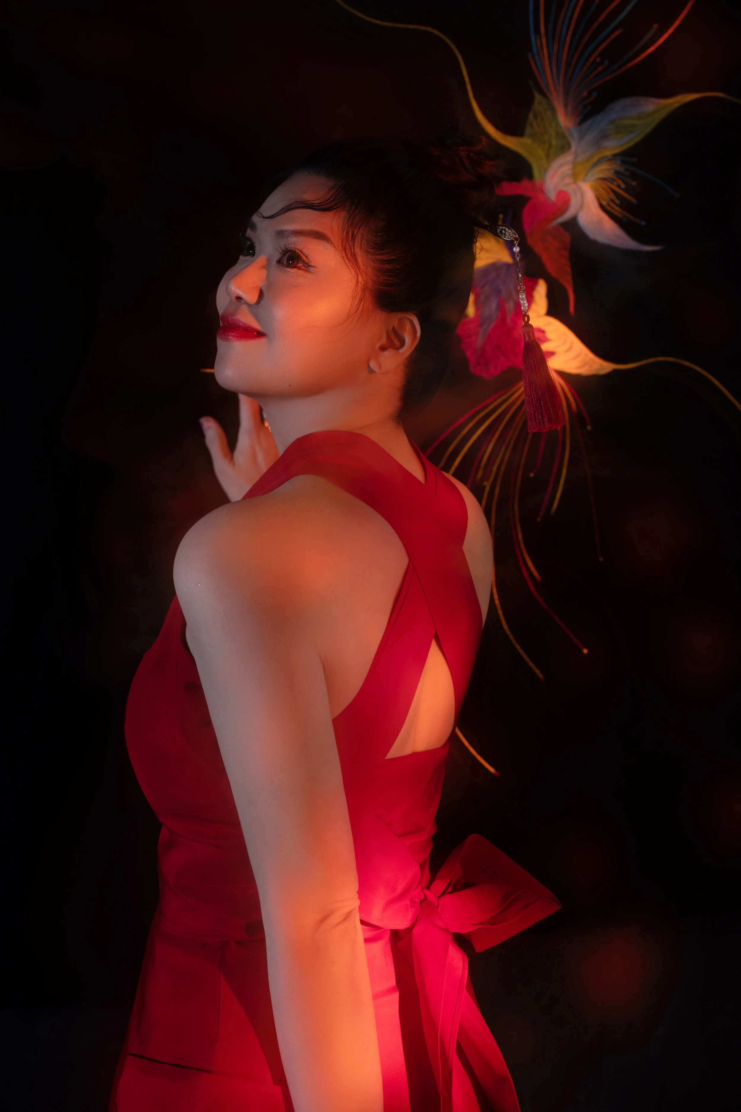 A woman in a red dress with a decorative hairpiece lies against a black background with colorful, illuminated floral patterns.