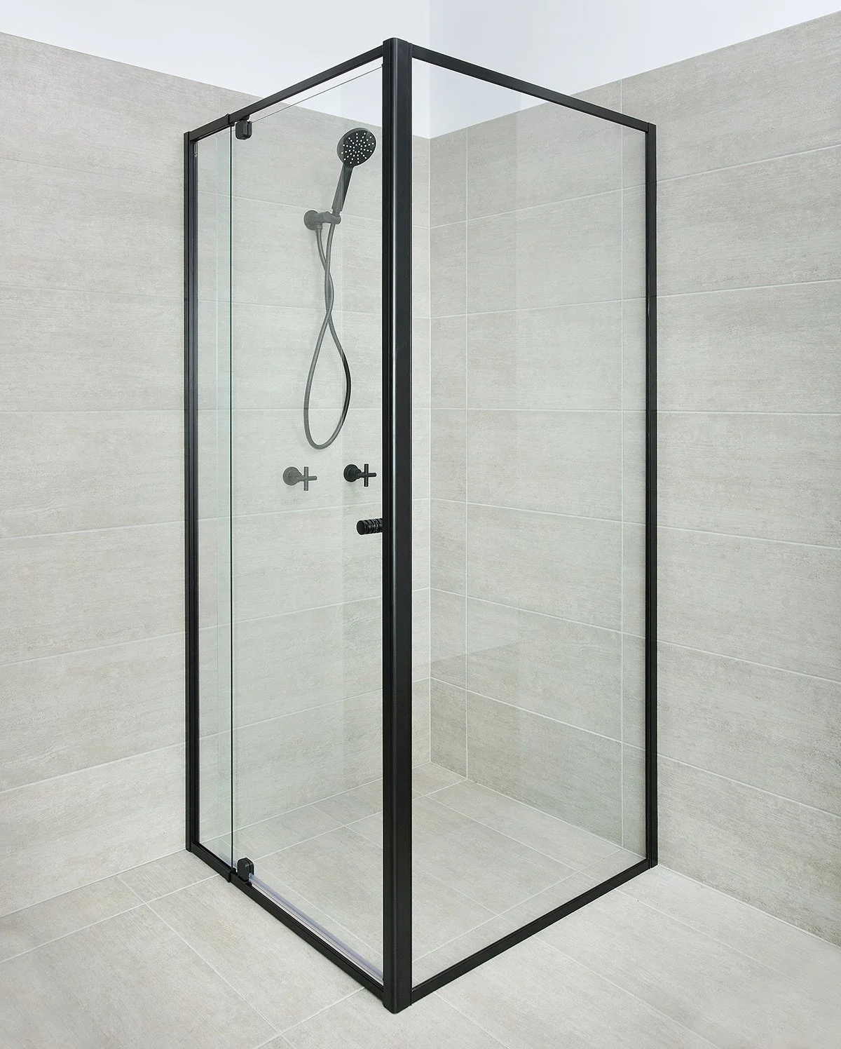 Minimalist glass shower enclosure with black metal frame, showerhead, and controls in a bathroom with light gray tiled walls and floor.