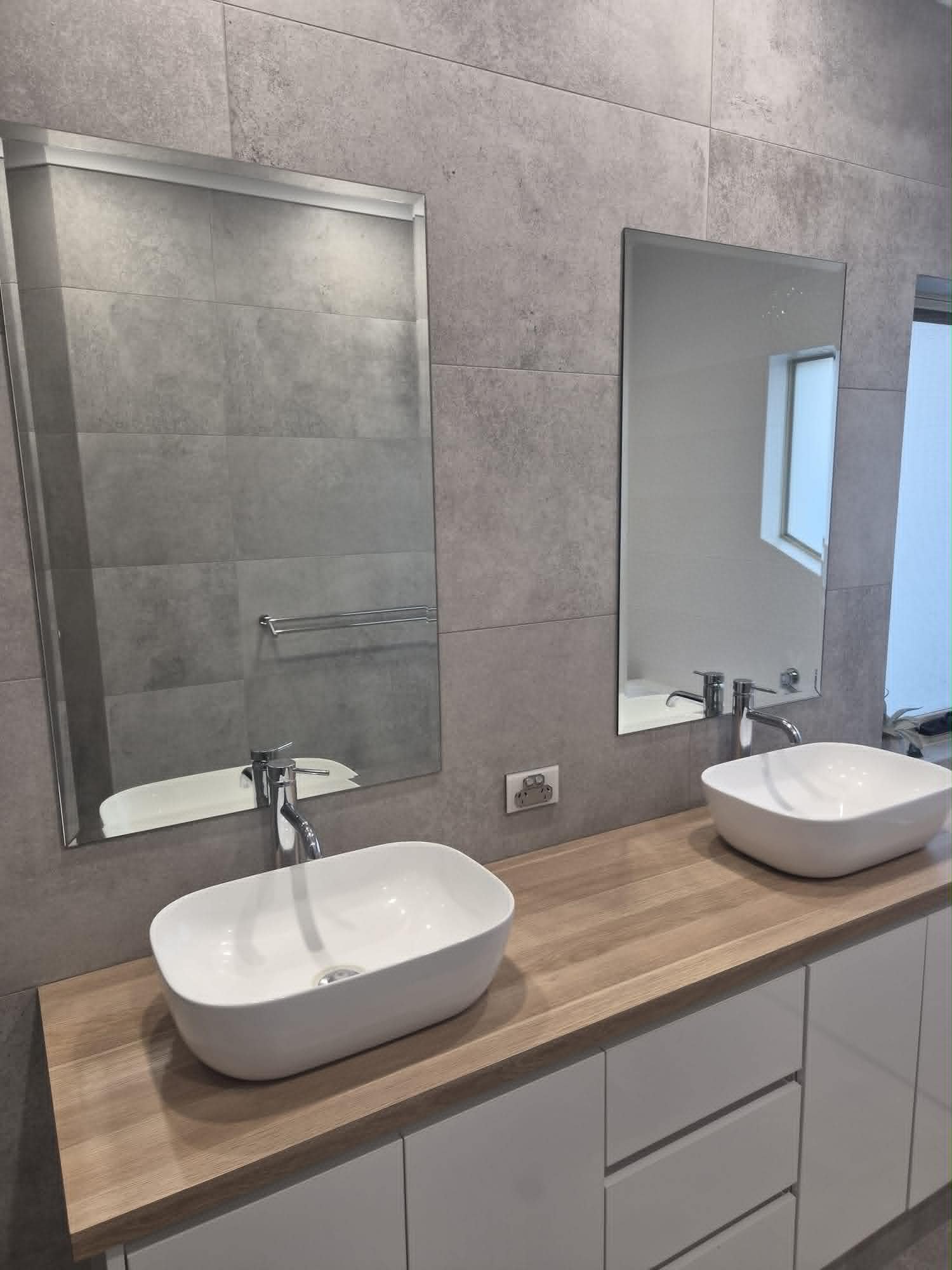 Bathroom with a double mirror, two vessel sinks on a wood countertop, towel bar, and a bidet, with a window and tiled walls.