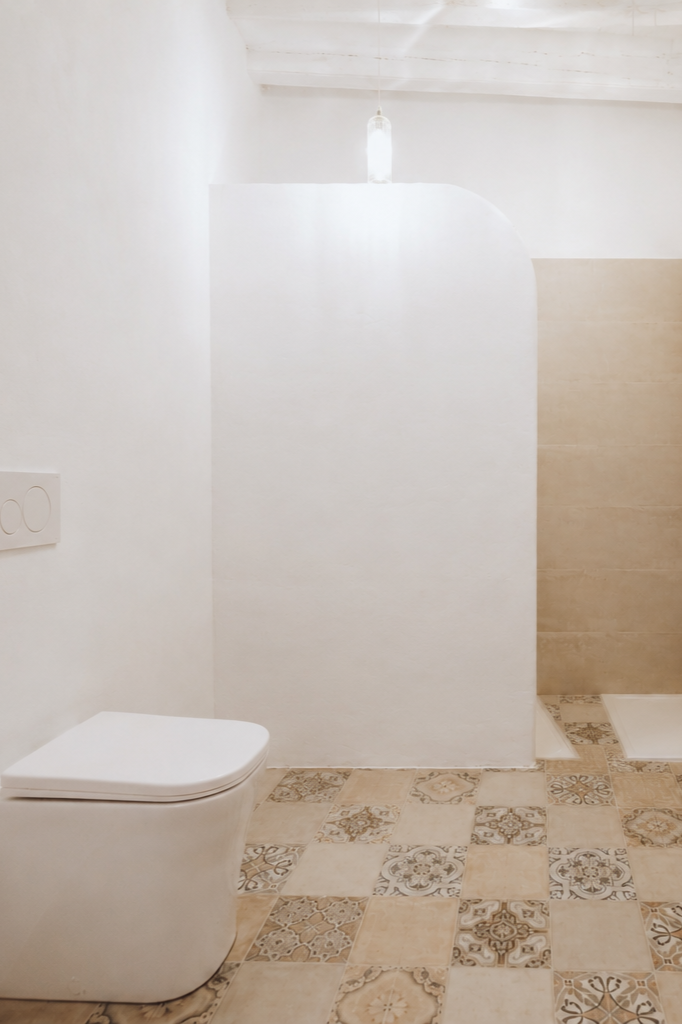 Modern minimalist bathroom with white walls, beige tiled floor with decorative patterns, and a wall-mounted toilet.