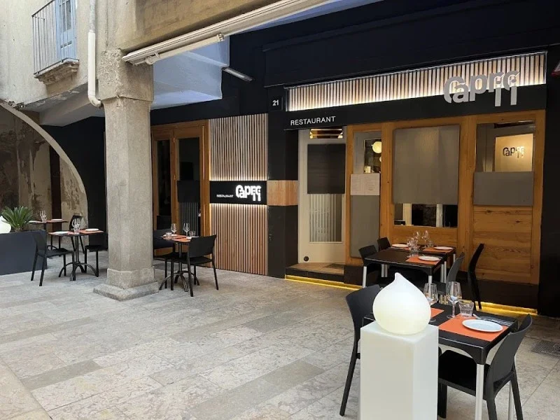 Exterior view of a restaurant named 'Capri' with outdoor seating, black and wood paneling, and a black door.