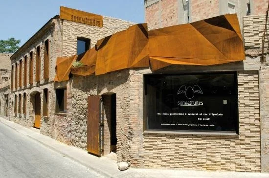 Historic brick building with modern rust-colored metal architectural accents and a large sign for "Somatrutes" on the facade.