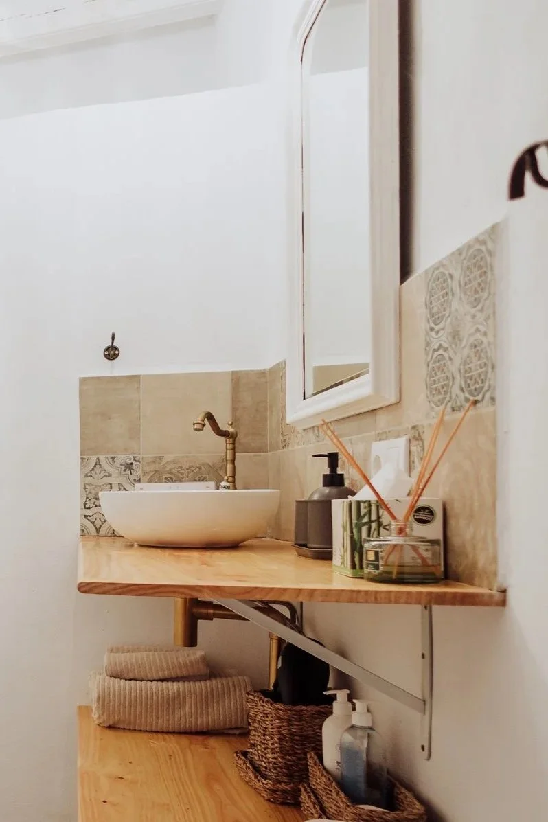 Bathroom vanity with a round vessel sink, faucet, mirror, and decorative tiles on the wall.