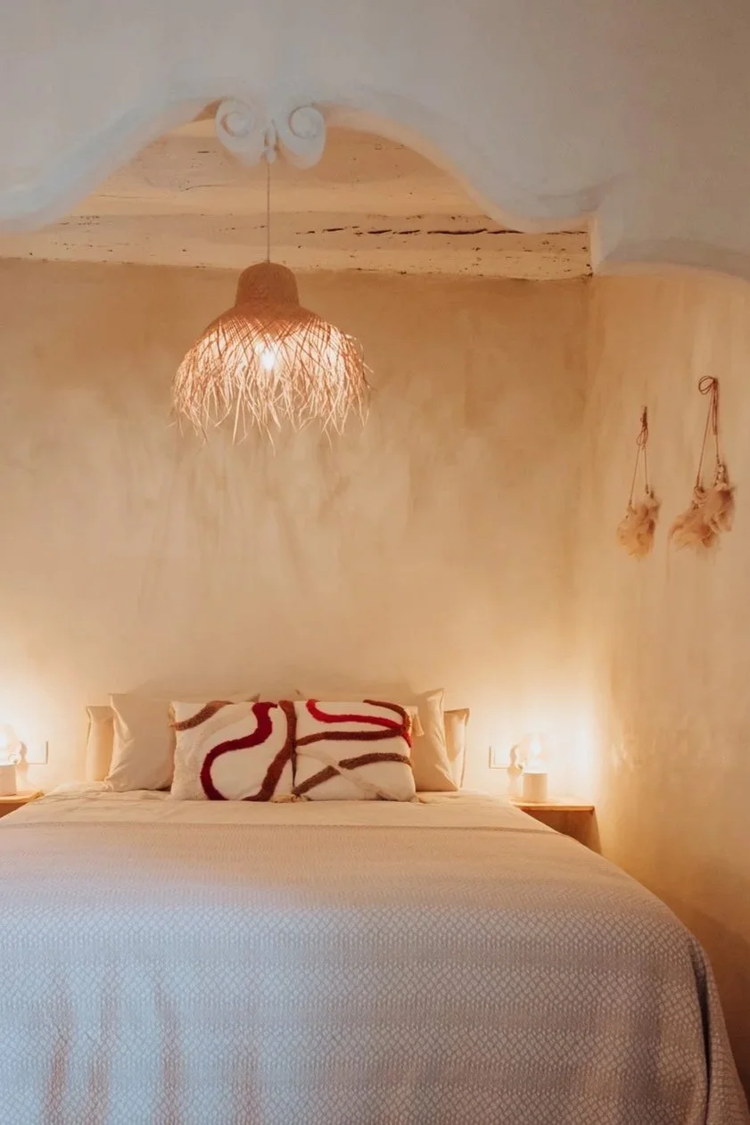 Cozy bedroom with a large bed, neutral-toned bedding, decorative pillows, bedside lamps, woven pendant light, and wall decor.