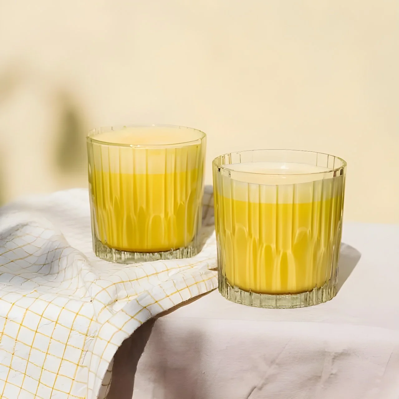 Two glasses of yellow-colored safra latte on a white surface with a white and yellow cloth.