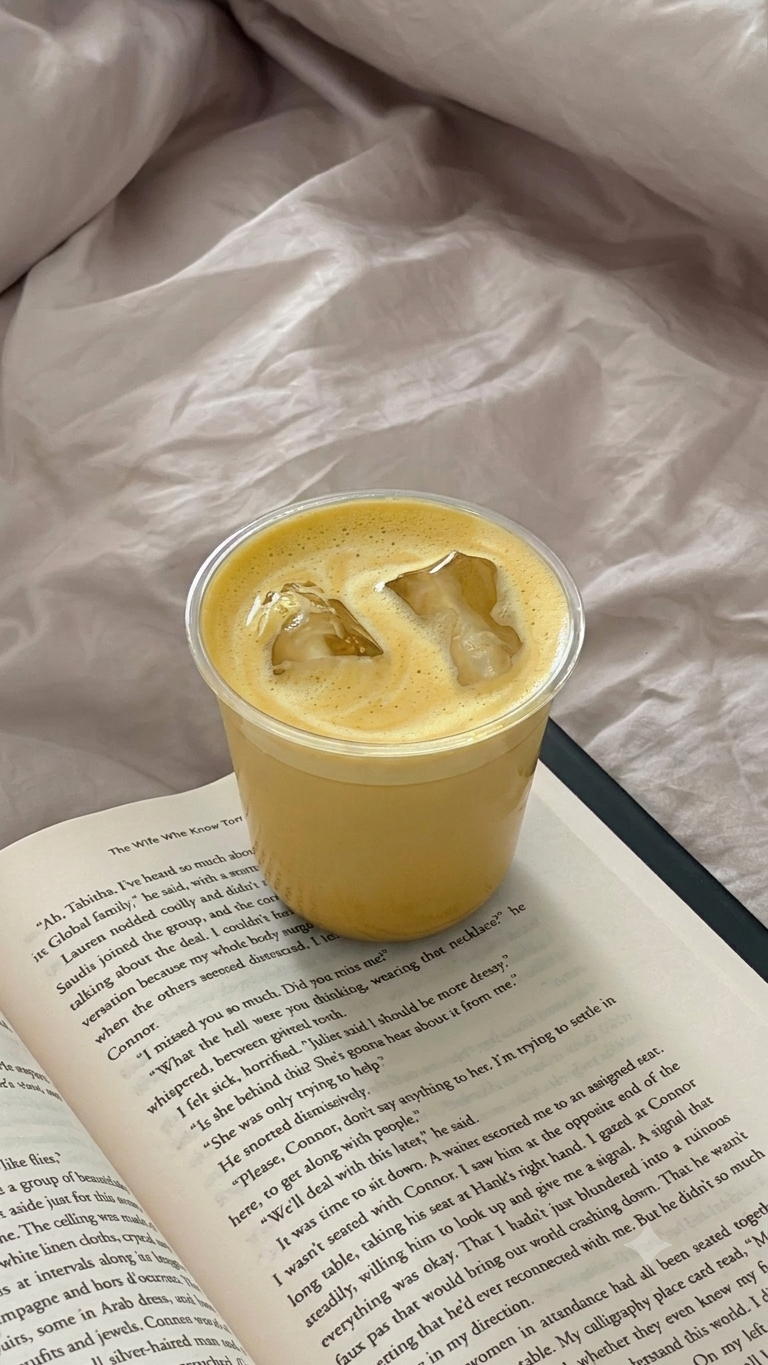 A cup of iced safra latte with ice cubes resting on an open book.
