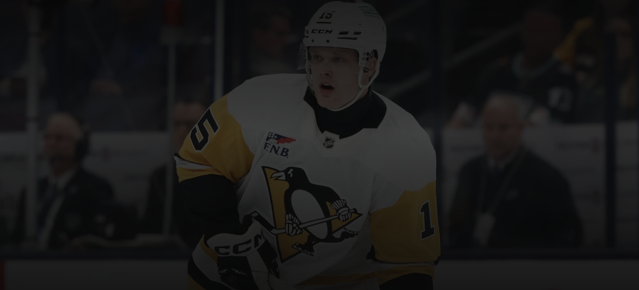 Jääkiekkoilija jääkiekkoareenalla, pukeutunut Pittsburgh Penguins -joukkueen pelipaitaan ja kypärään, katsoo eteenpäin.