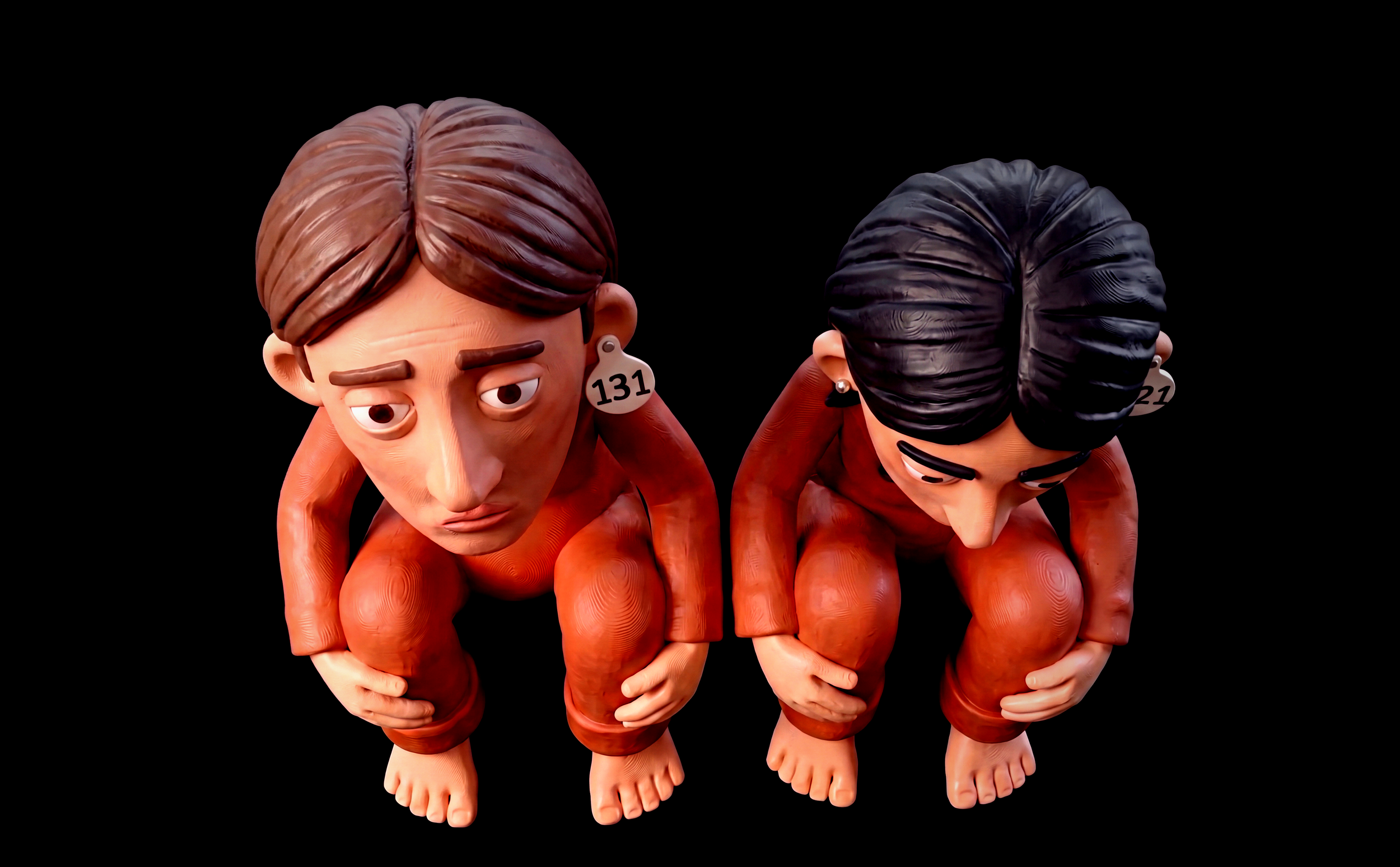 Two figurines of people in orange outfits with large heads and exaggerated features, kneeling and bending forward with hands on their knees, against a black background.