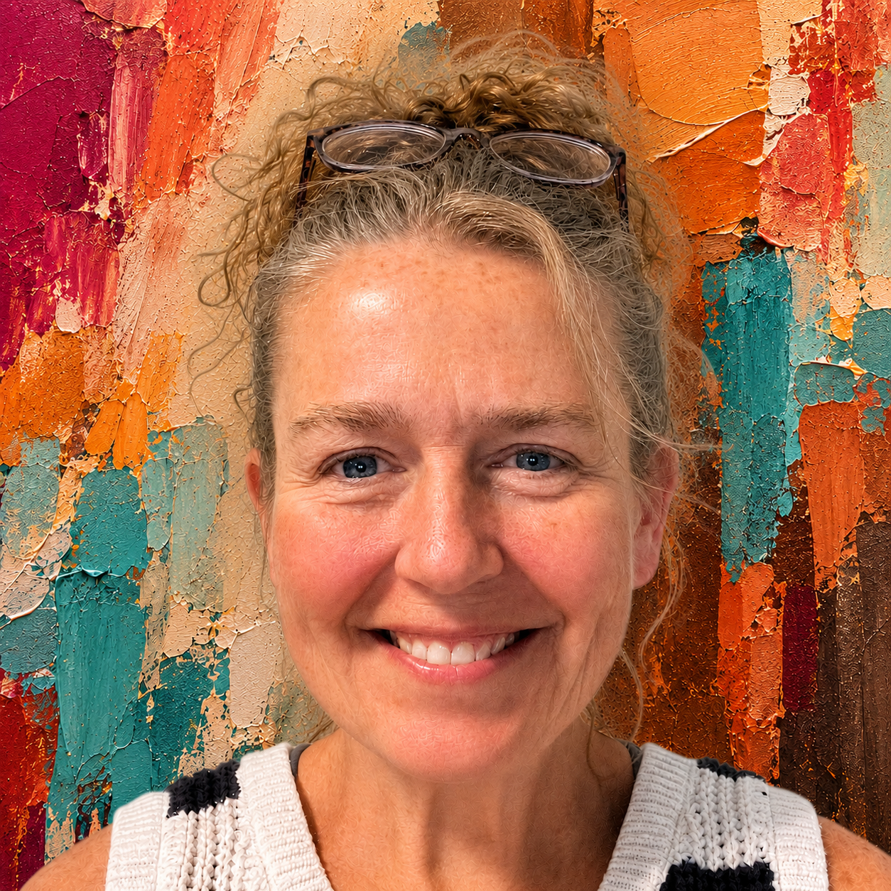 A woman smiling in front of an abstract textured painting with orange, teal, and red hues, wearing glasses on her head and a white knitted top.