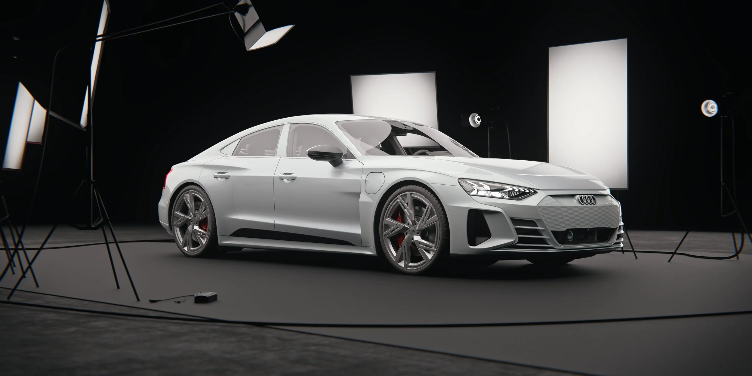 Silver Audi e-tron GT in front three-quarter view inside a photography studio with softboxes and lighting stands. Silberner Audi e-tron GT in Dreiviertelansicht von vorn in einem Fotostudio mit Softboxen und Lichtstativen.