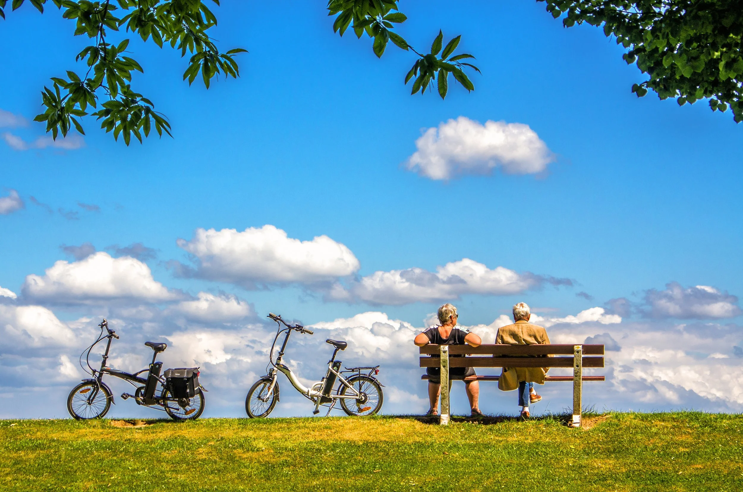 Couple sat on bench, on sunny day, next to their bicycles