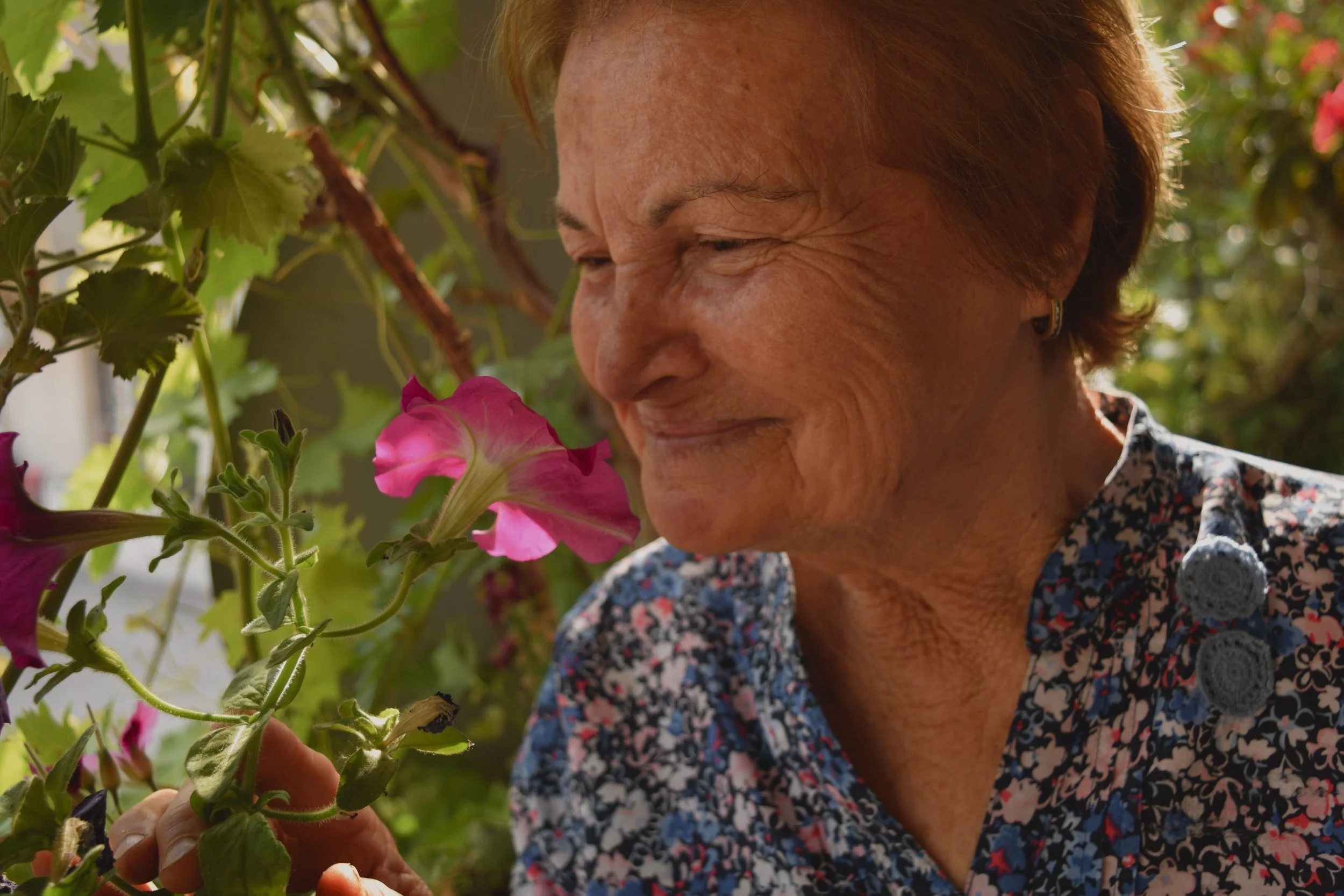 Older woman enjoying flowers in a garden.
