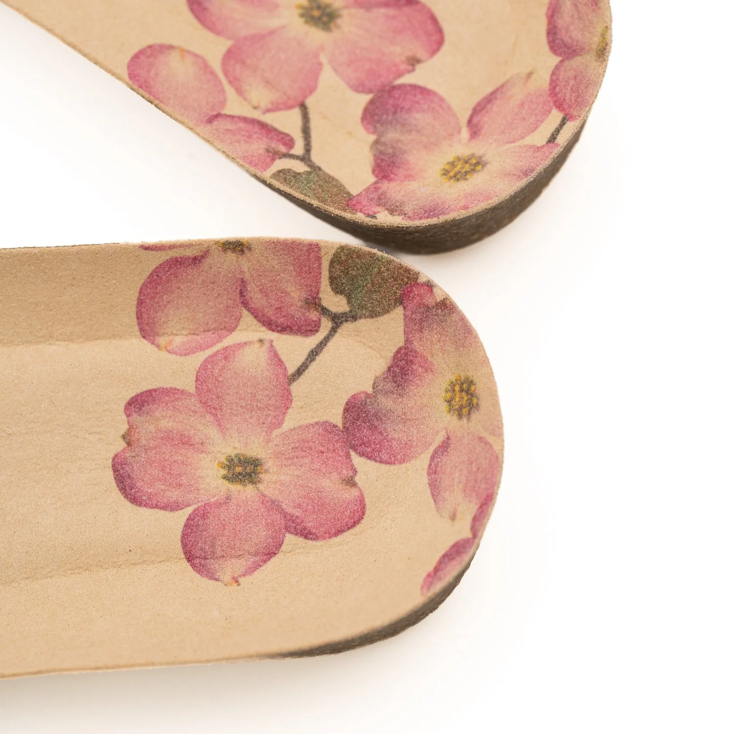 Zapatillas de color beige con dibujo de flores rosadas y fondo blanco.