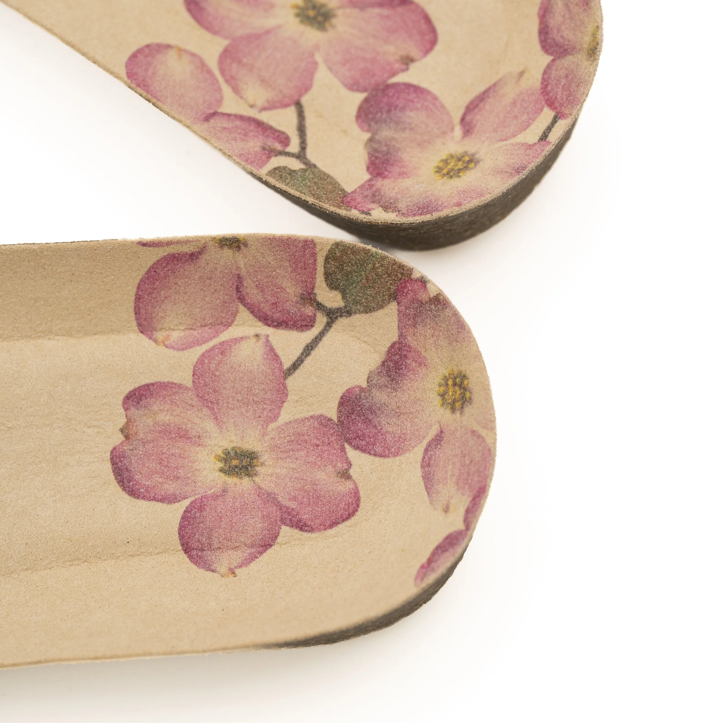 Cerca de una bolsa de papel de color marrón claro con flores rosadas y centros amarillos, hay papel de burbujas de aire y una superficie blanca.