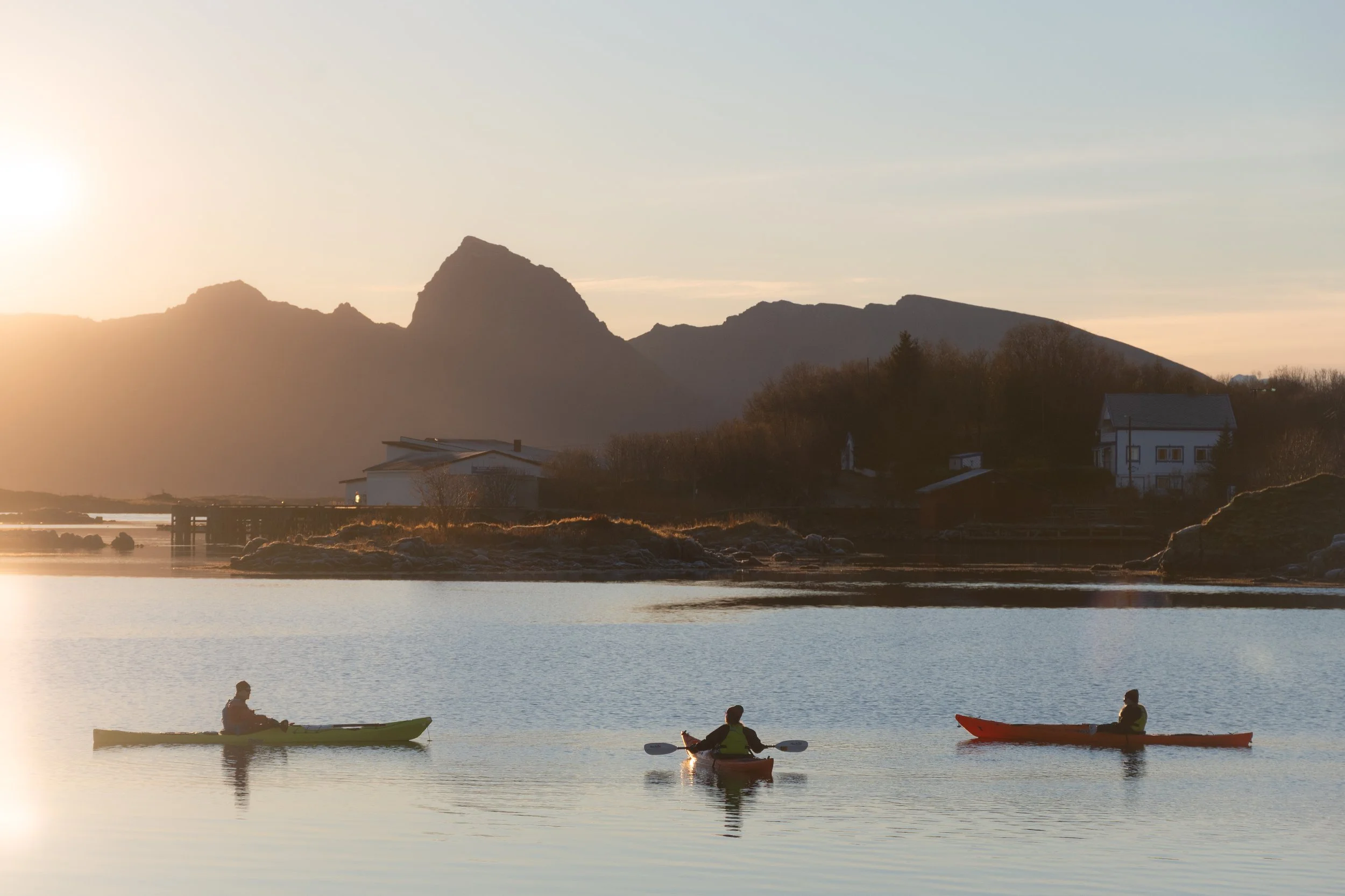Three kayakers on a guided trip in golden light with autumn colours in Ringstad harbour