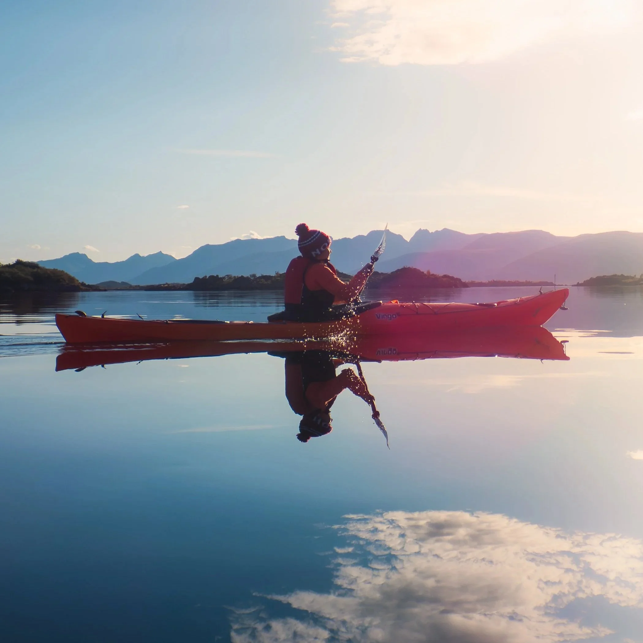 Lone kayaker paddling across mirror smooth water in Vesterålen