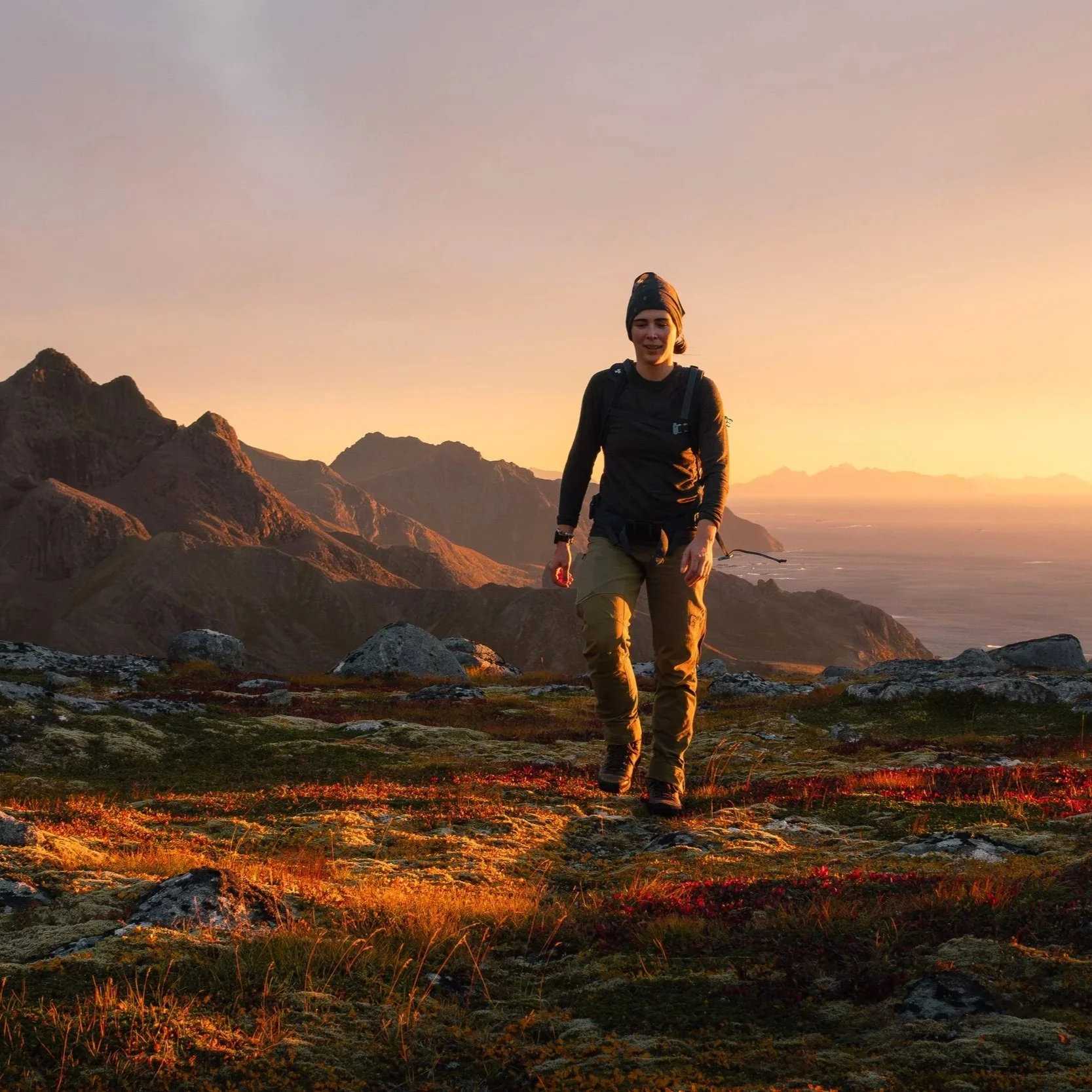 Lady walking towards the camera on a mountain with golden sunset bathing the dramatic mountain landscape behind