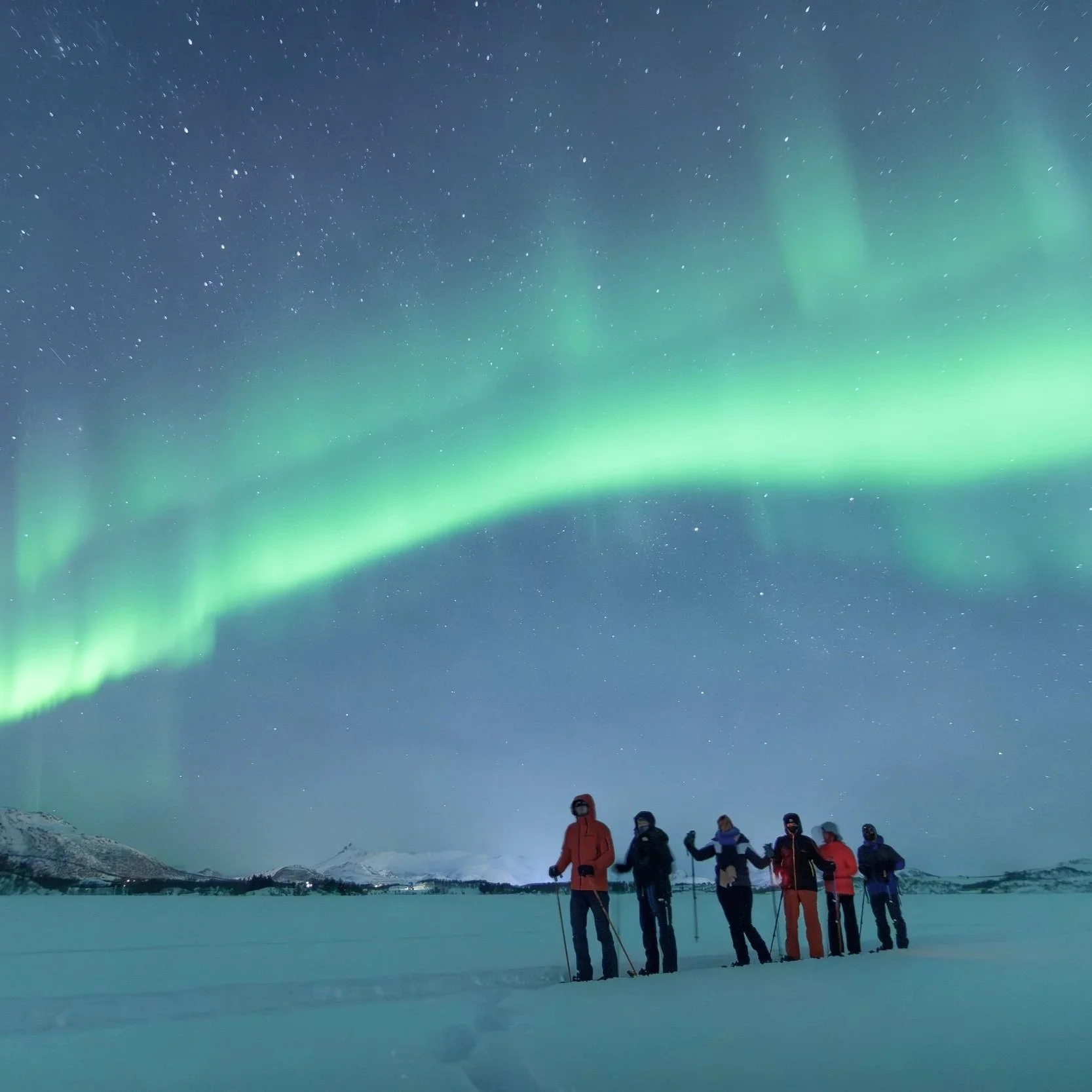 Guided snowshoe group walking across a frozen lake with the northern lights overhead