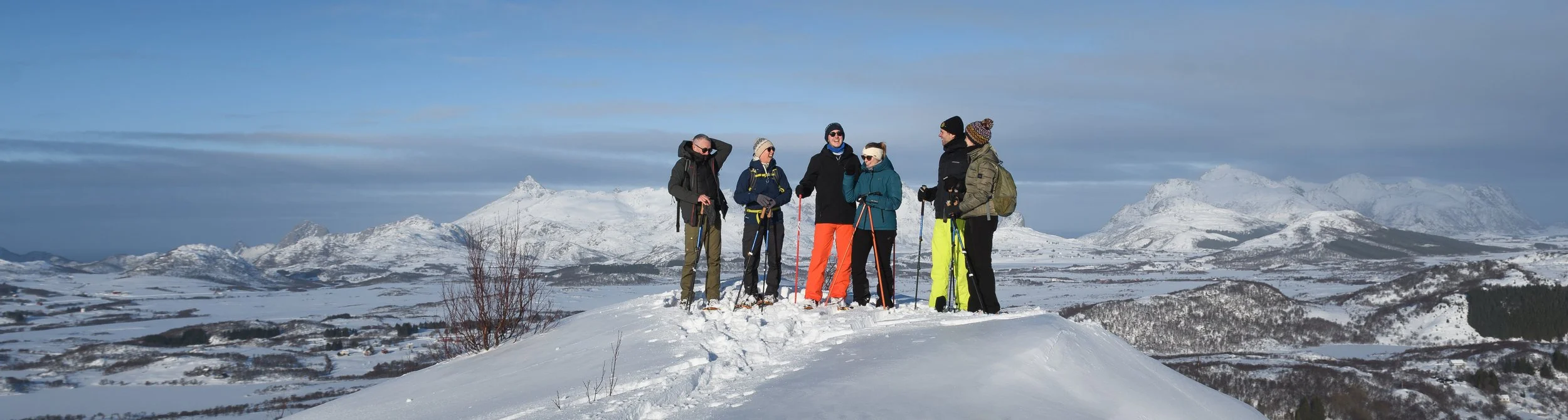 Guided snowshoe group laughing on a mountain summit with a backdrop of snow covered mountains