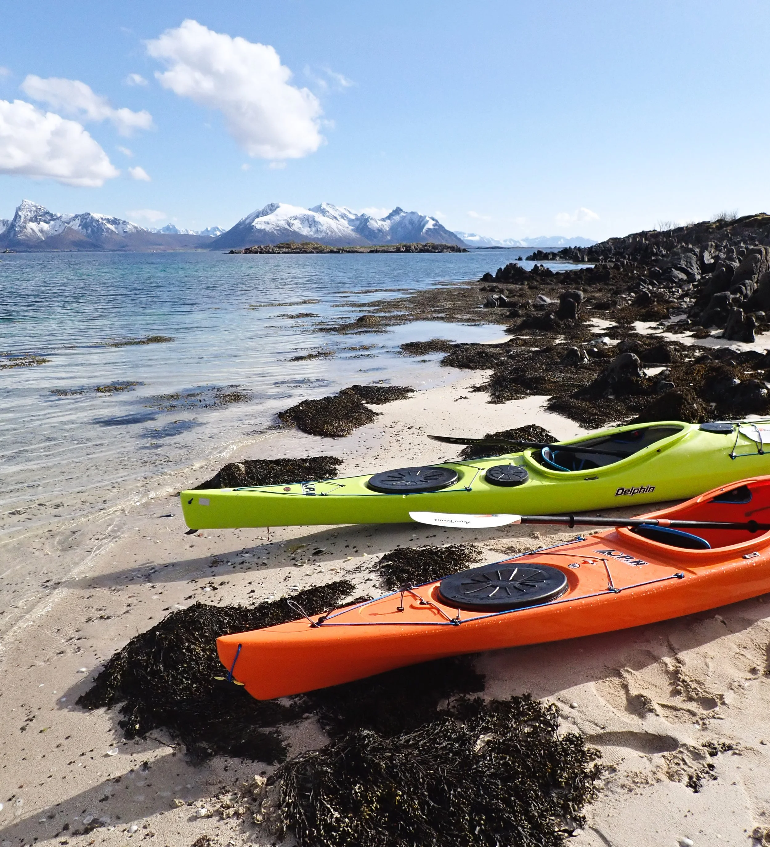 Two kayaks on a white sand beach in the sun with mountains behind